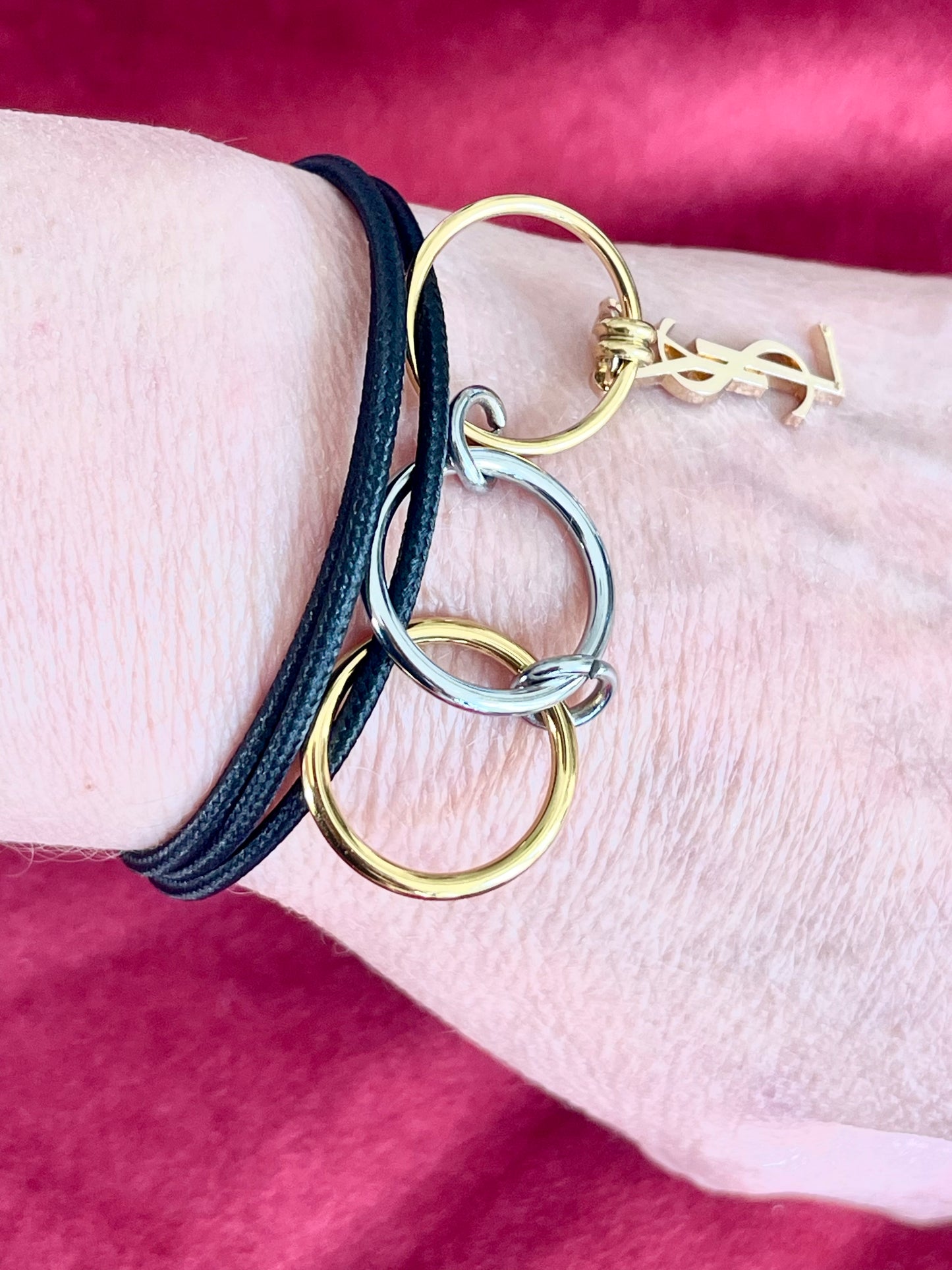 Worn as a bracelet On hand close up view Yves Saint Laurent authentic charm as a ring pendant and bracelet with magnetic black cord stainless steel gold silver tone