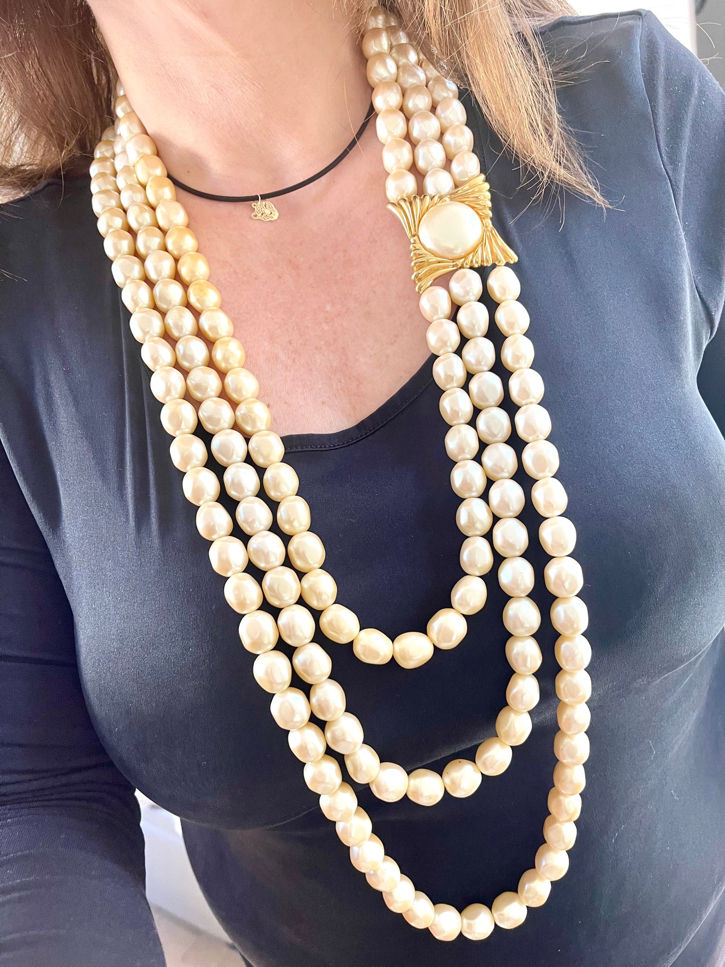 Close-up of YSL faux pearl necklace clasp worn on neck, highlighting the gold-tone sculptural design and domed pearl centerpiece