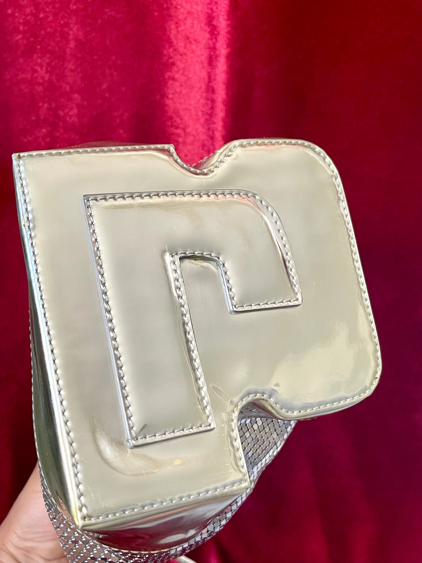 Bottom view of Paco Rabanne silver shoulder/wrist bag with both straps shown, on red velvet fabric background.