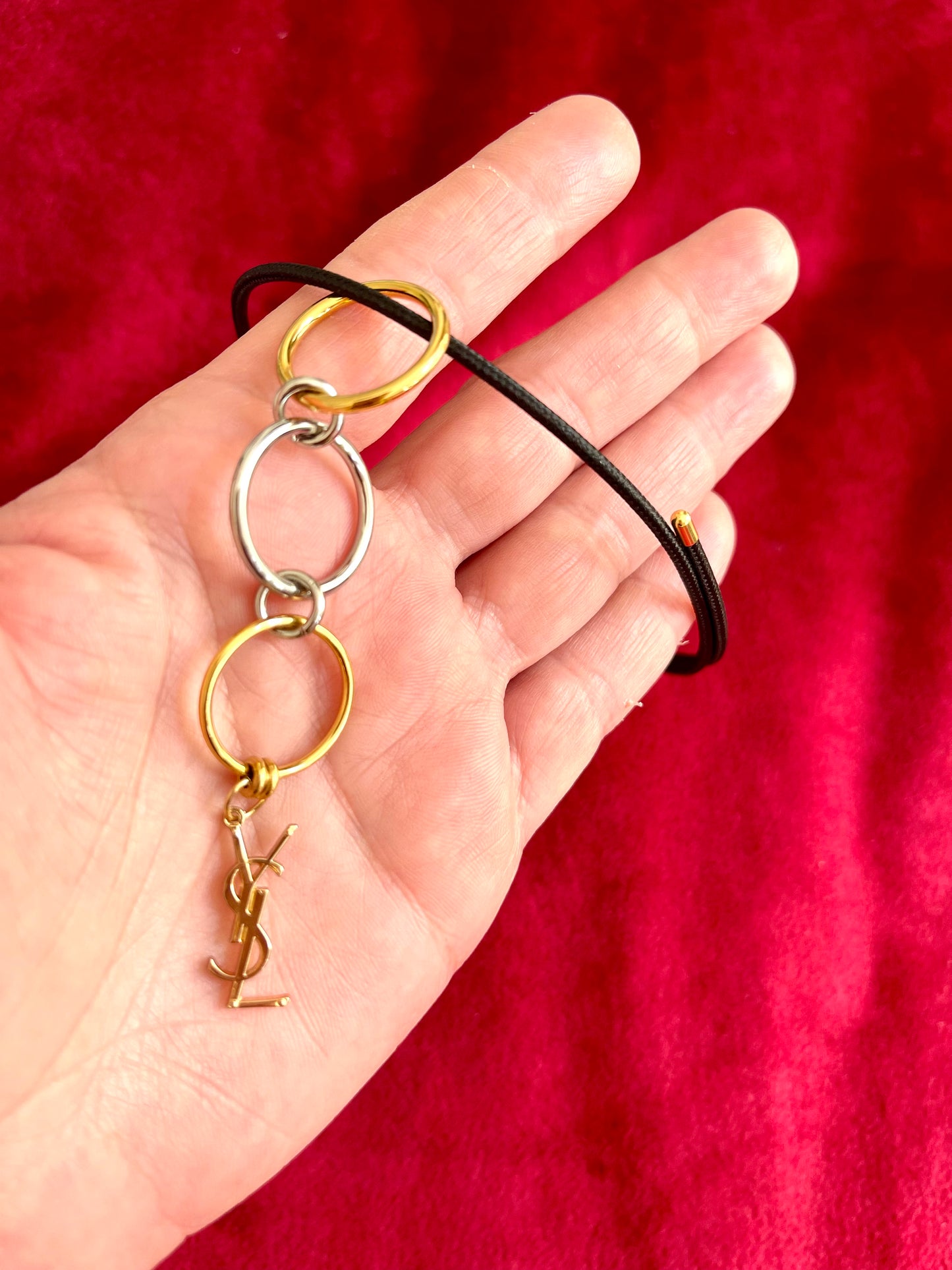 On hand On hand close up view Yves Saint Laurent authentic charm as a ring pendant and bracelet with magnetic black cord stainless steel gold silver tone