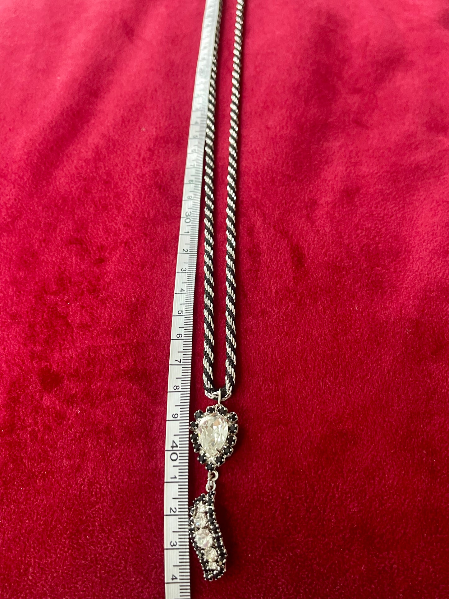 Using a measuring tape 44 cm long , vintage Trifari silver tone black cord necklace with Christian Dior pendant on a red background