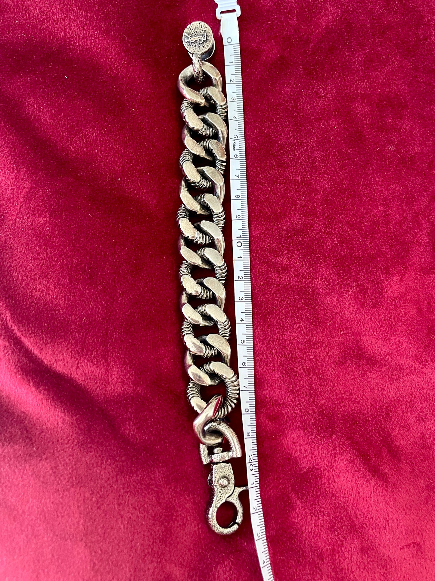 Using a measuring tape Top view Preloved YSL bronze and grey chain worn as a statement piece against red velvet background