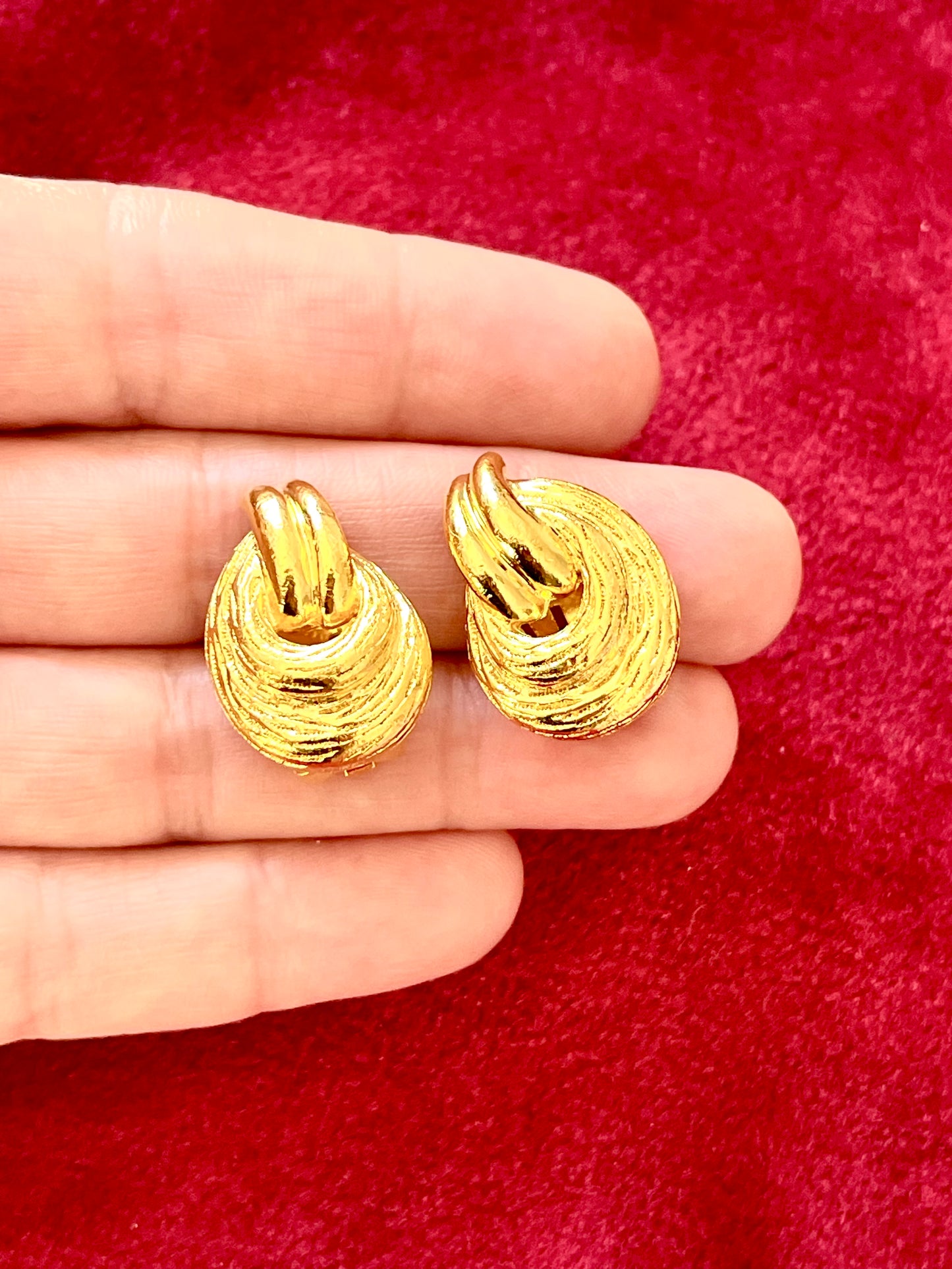On hand Vintage Christian Dior clip on Dior earrings, gold plated 18KG displayed on a red velvet background