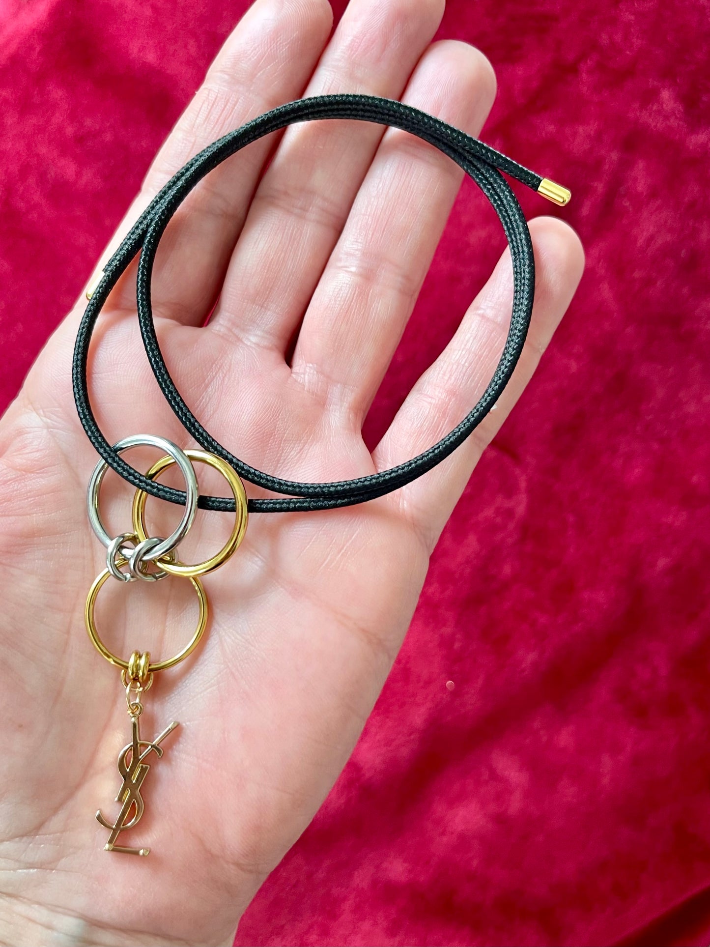 On hand close up view Yves Saint Laurent authentic charm as a ring pendant and bracelet with magnetic black cord stainless steel gold silver tone