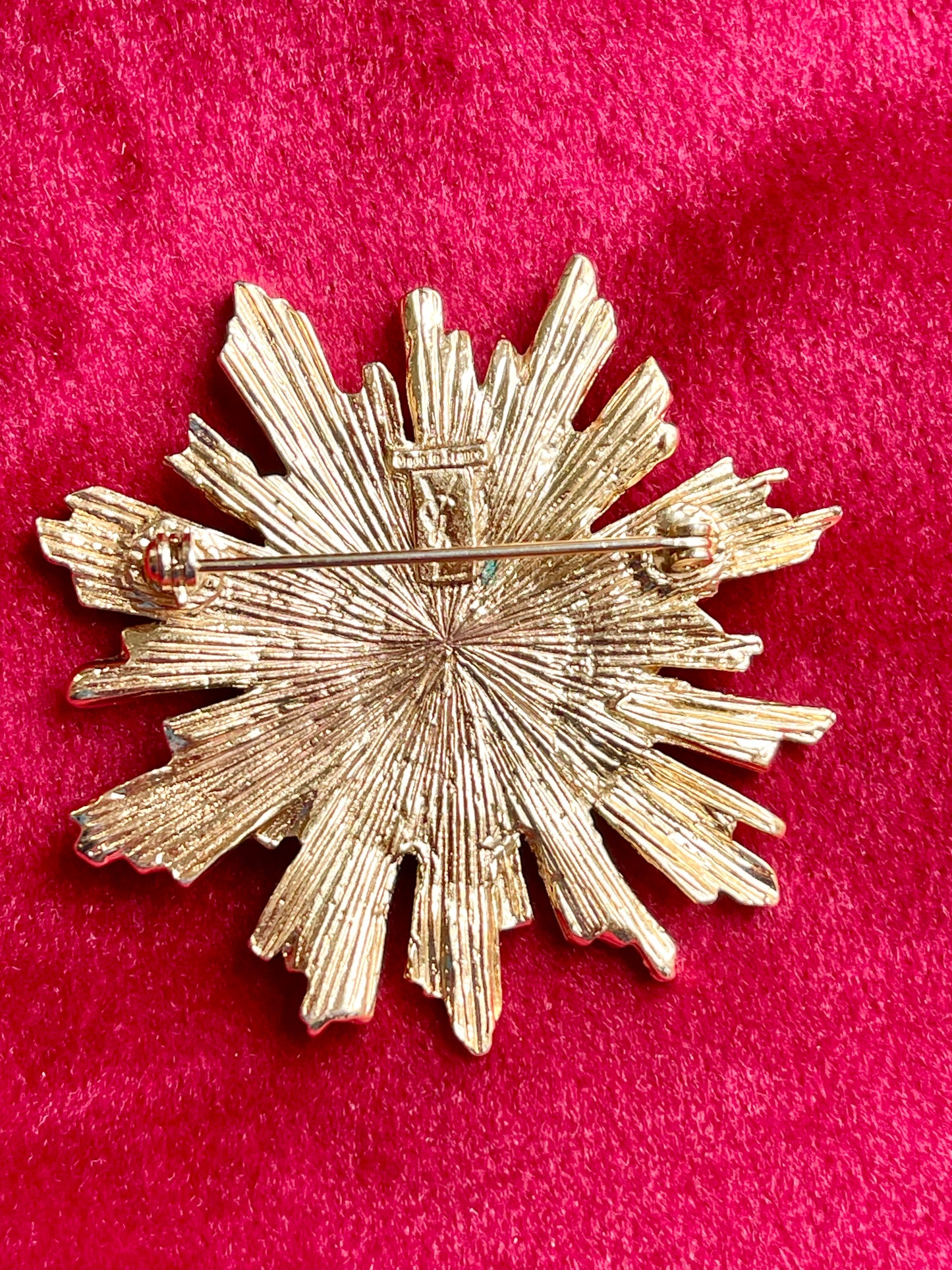 Back view Vintage Yves Saint Laurent 1980s gold-tone sunburst brooch with green cabochon center on red velvet background