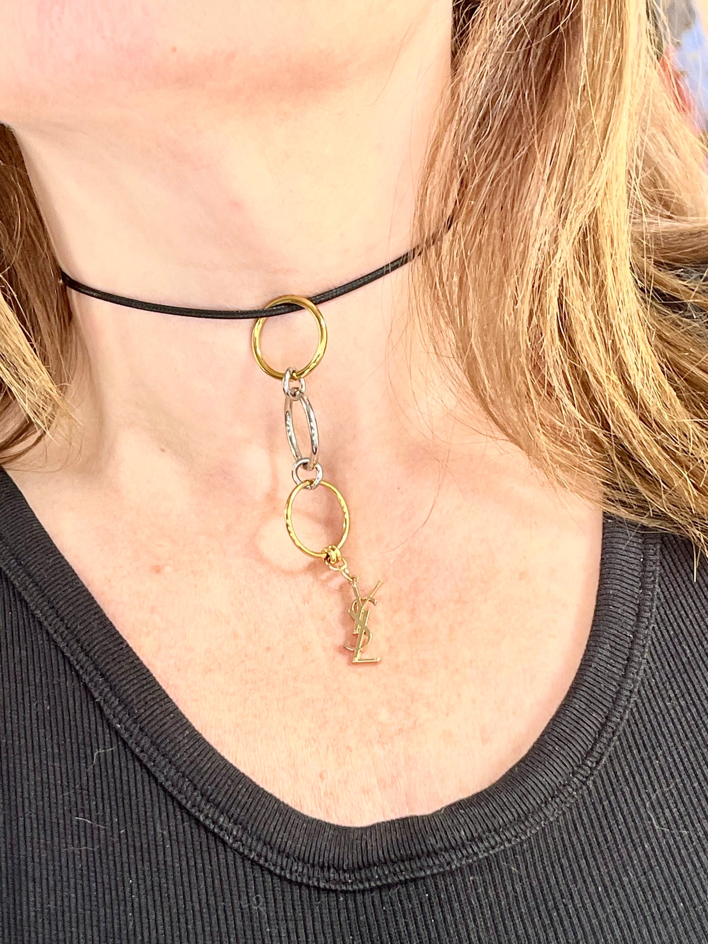Differently worn close up view Yves Saint Laurent authentic charm as a ring pendant and bracelet with magnetic black cord stainless steel gold silver tone