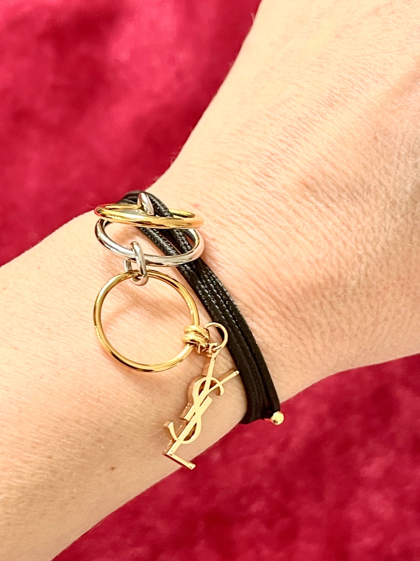 On hand close up view Yves Saint Laurent authentic charm as a ring pendant and bracelet with magnetic black cord stainless steel gold silver tone