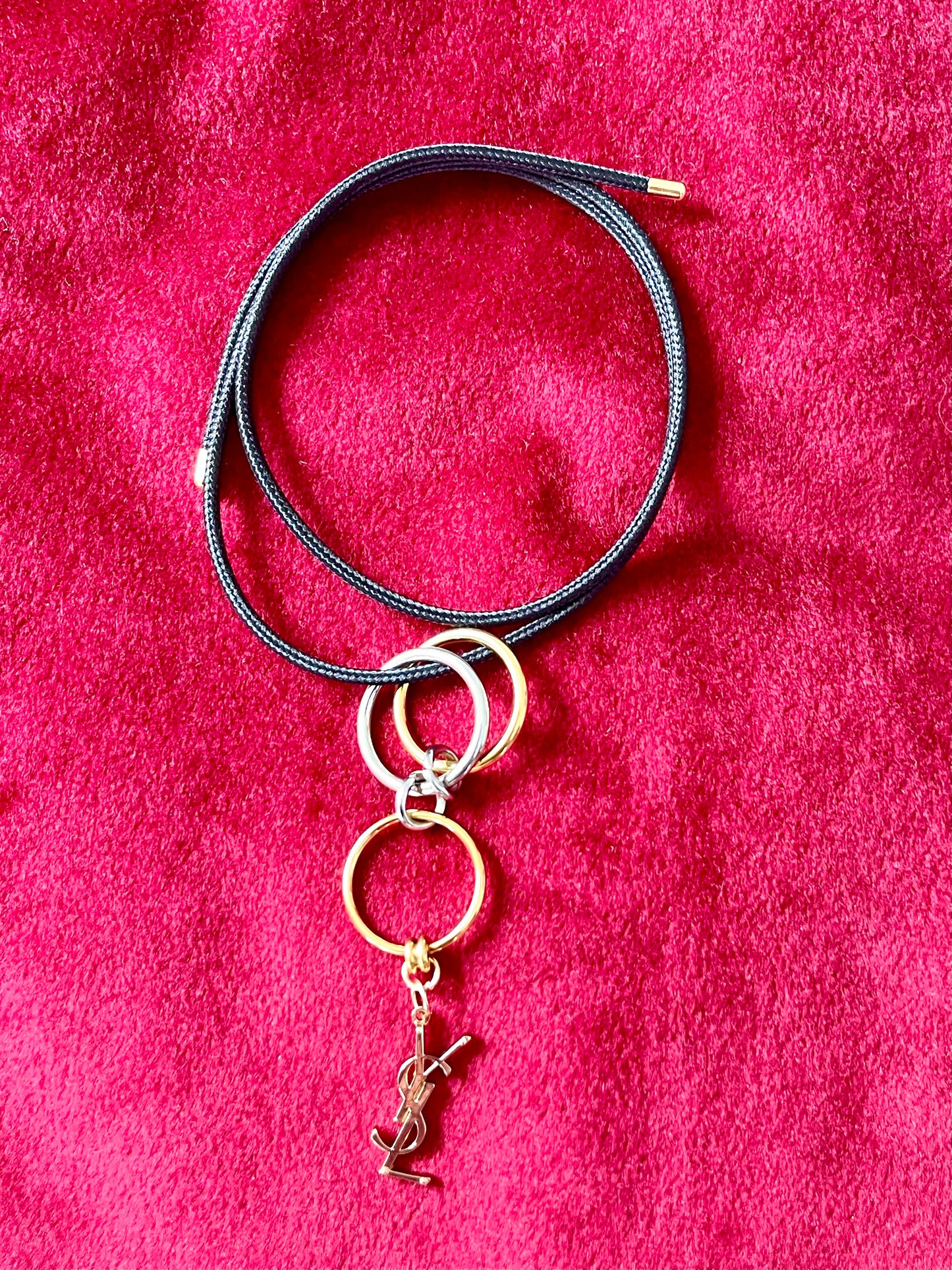 Yves Saint Laurent authentic charm as a ring pendant and bracelet with magnetic black cord stainless steel gold silver tone on a red velvet background