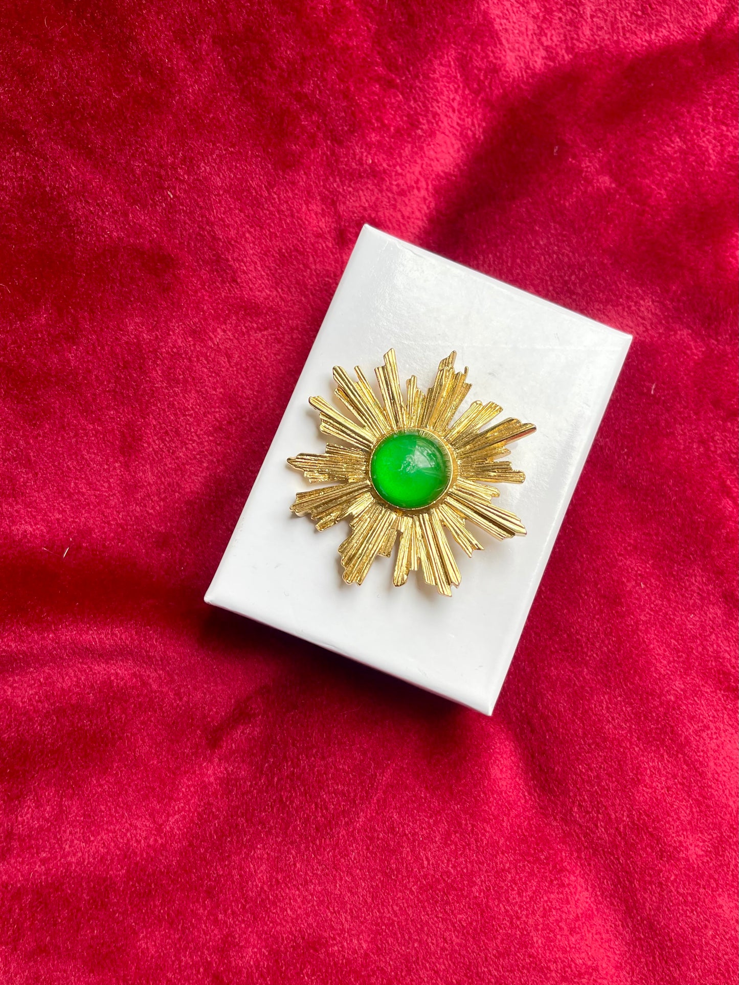 Vintage Yves Saint Laurent 1980s gold-tone sunburst brooch with green cabochon center on white display