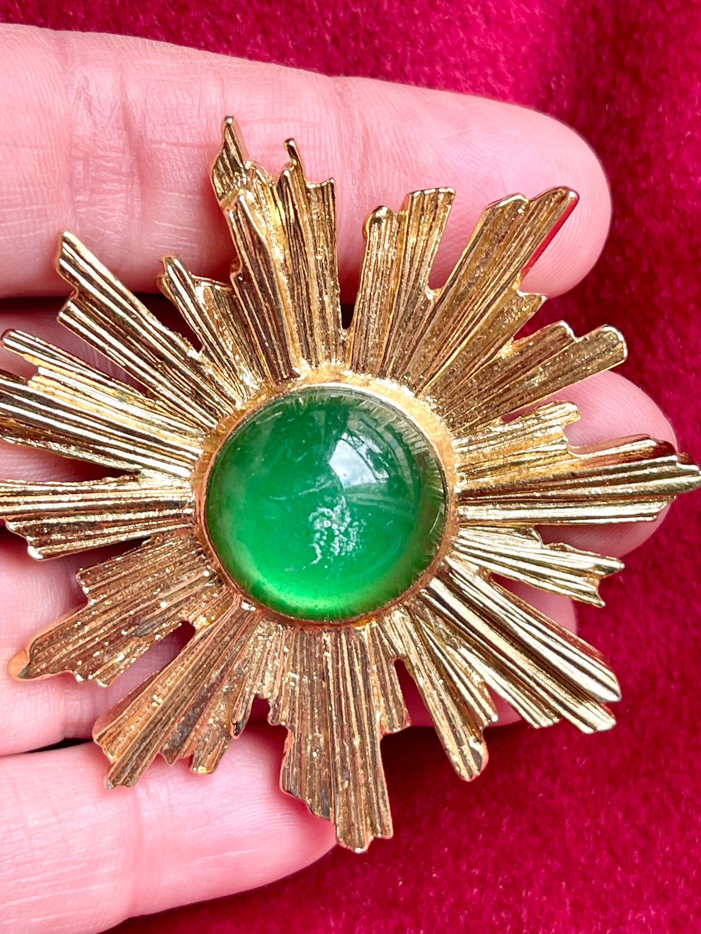 Vintage Yves Saint Laurent 1980s gold-tone sunburst brooch with green cabochon center displayed on hand