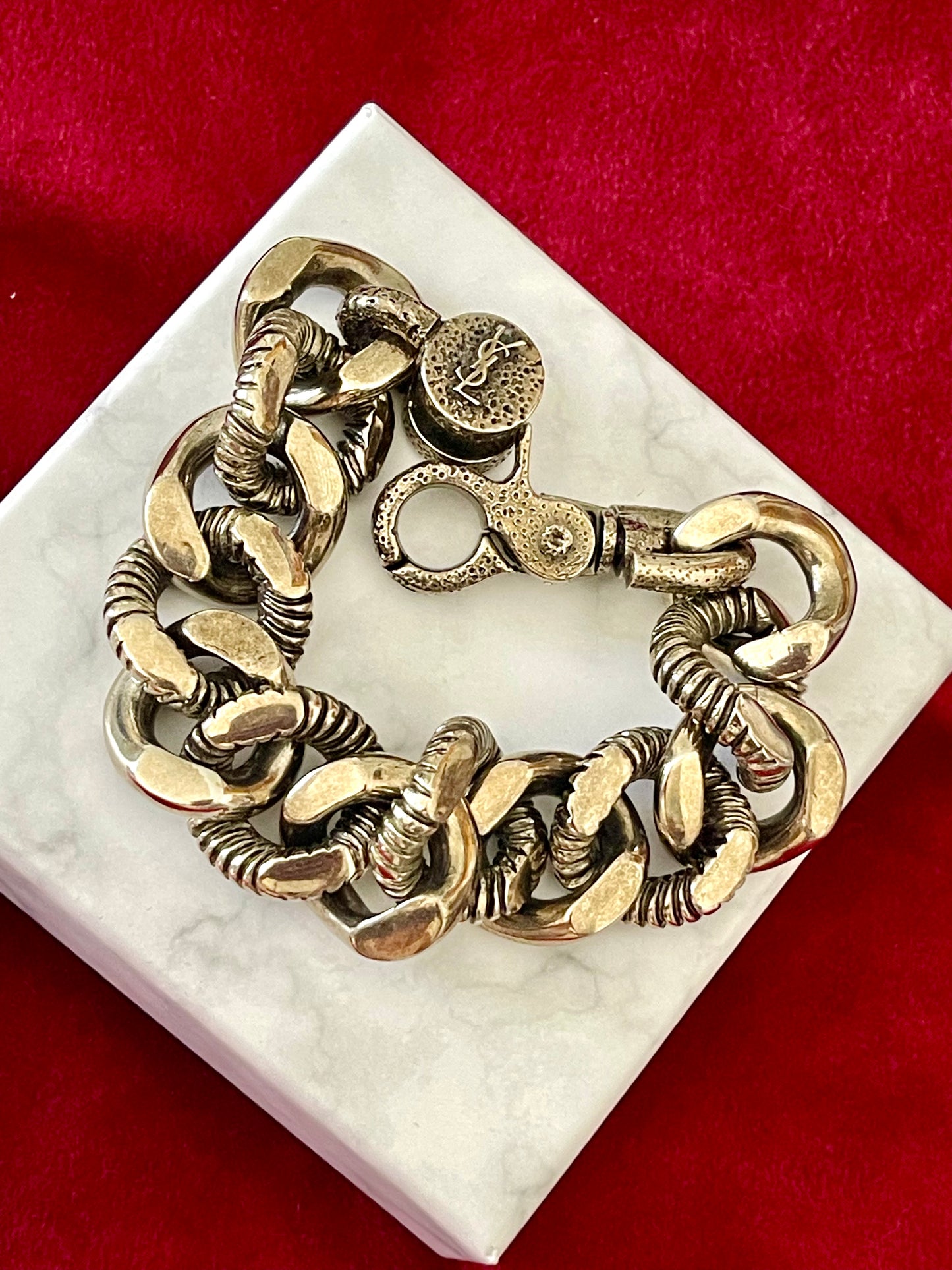 Close up view Preloved YSL bronze and grey chain worn as a statement piece against white background with red velvet