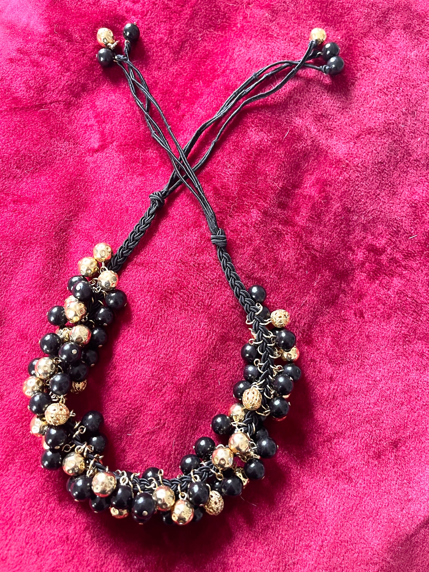 Vintage Yves Saint Laurent beaded necklace with black and gold beads, woven into braided black cotton cords, displayed on a red velvet background