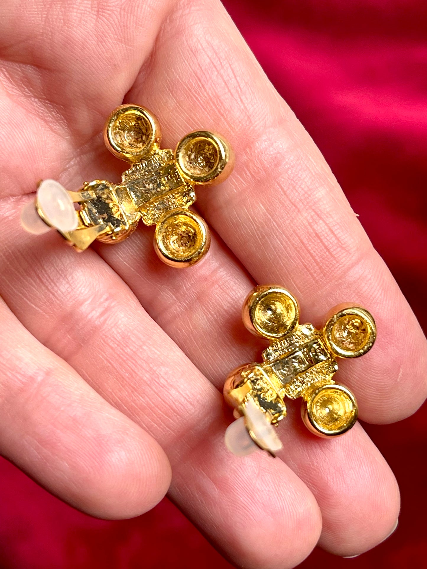 Yves Saint Laurent vintage gold tone cross clip-on earrings from the 1980s held in hand, showing rounded gold domes , square-cut center stones , YSL stamp engraved