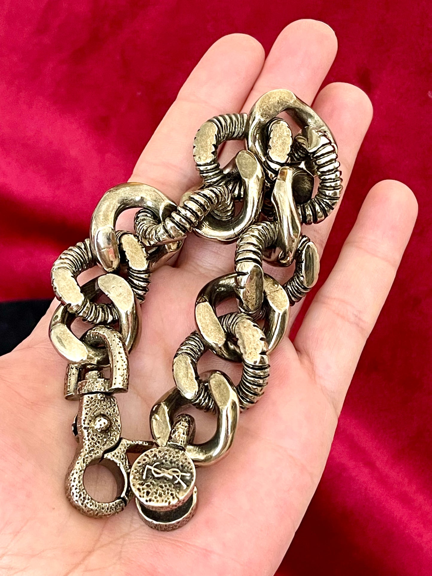 Laying flat on hand Preloved YSL bronze and grey chain worn as a statement piece against black fabric and YSL pouch