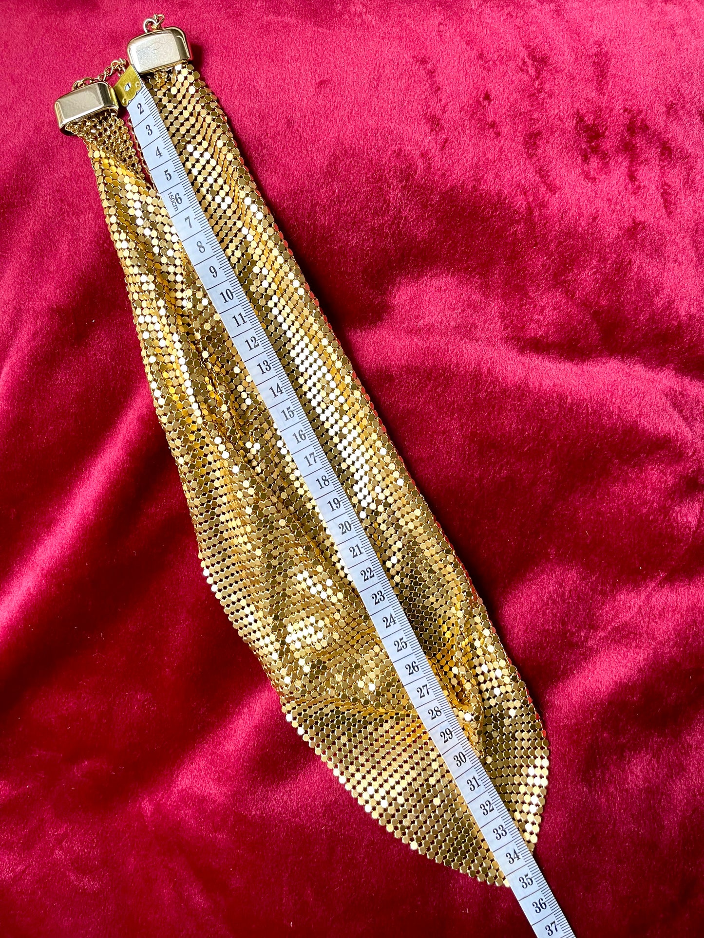 Gold tone metal Pixel scarf necklace Paco Rabanne style on red background using measuring tape