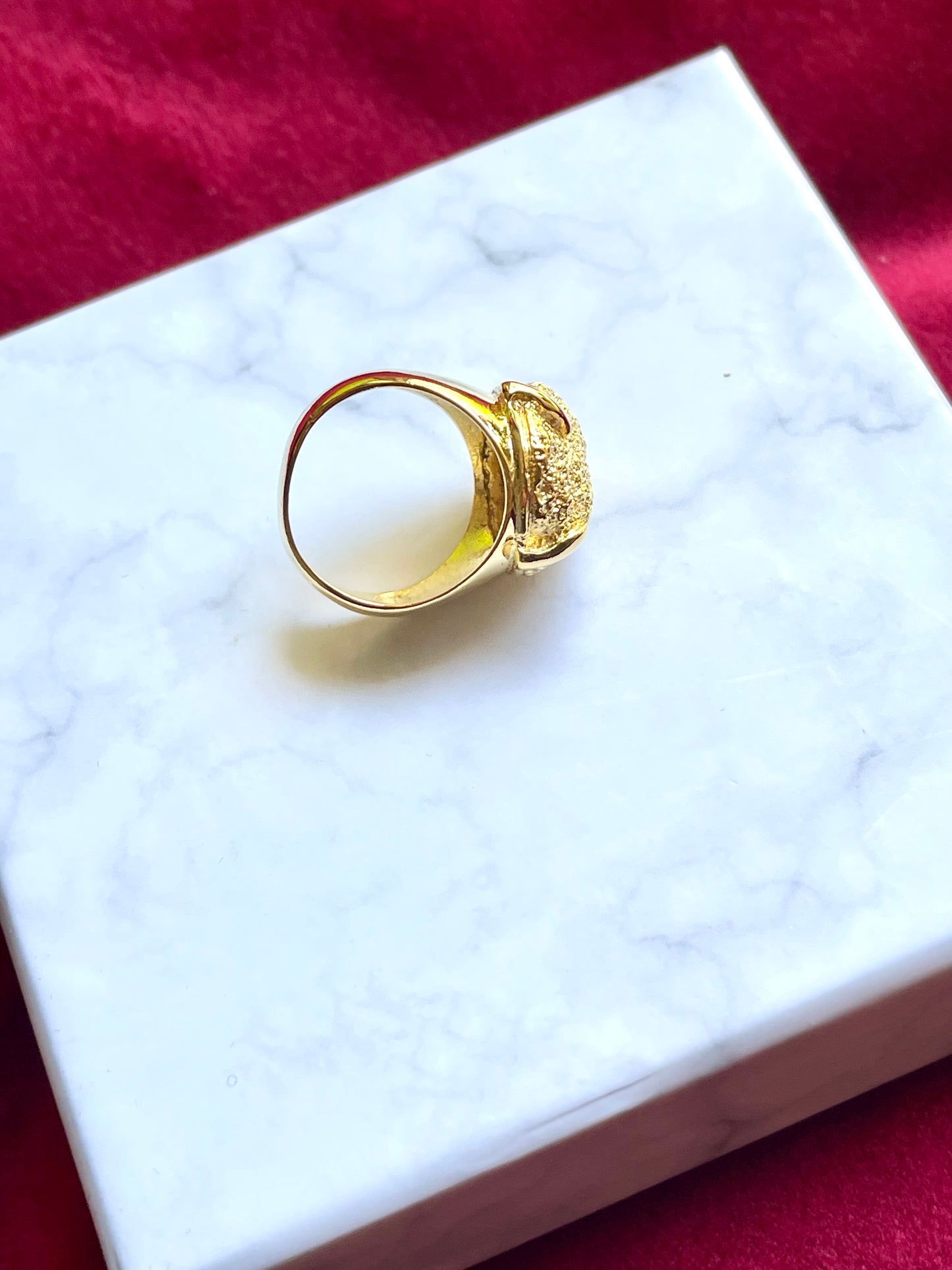 Profile view of the vintage Yves Saint Laurent ring placed on red velvet, showing the sculptural band and polished 18K gold plating