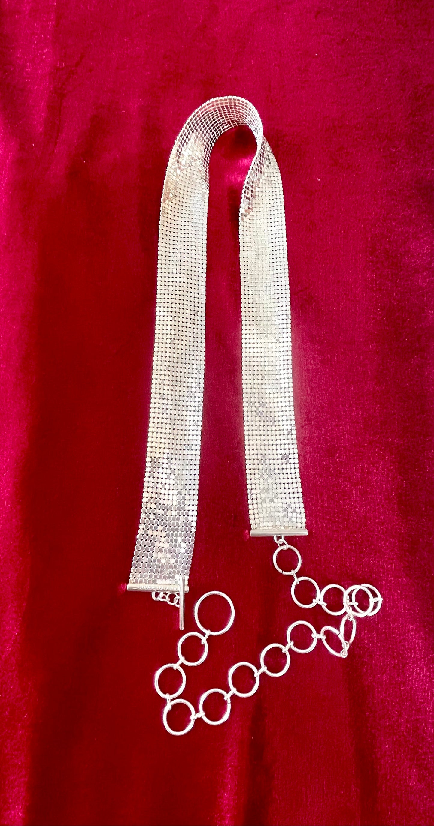 Flat lay of vintage silver Paco Rabanne mesh belt with hoops on red velvet background.