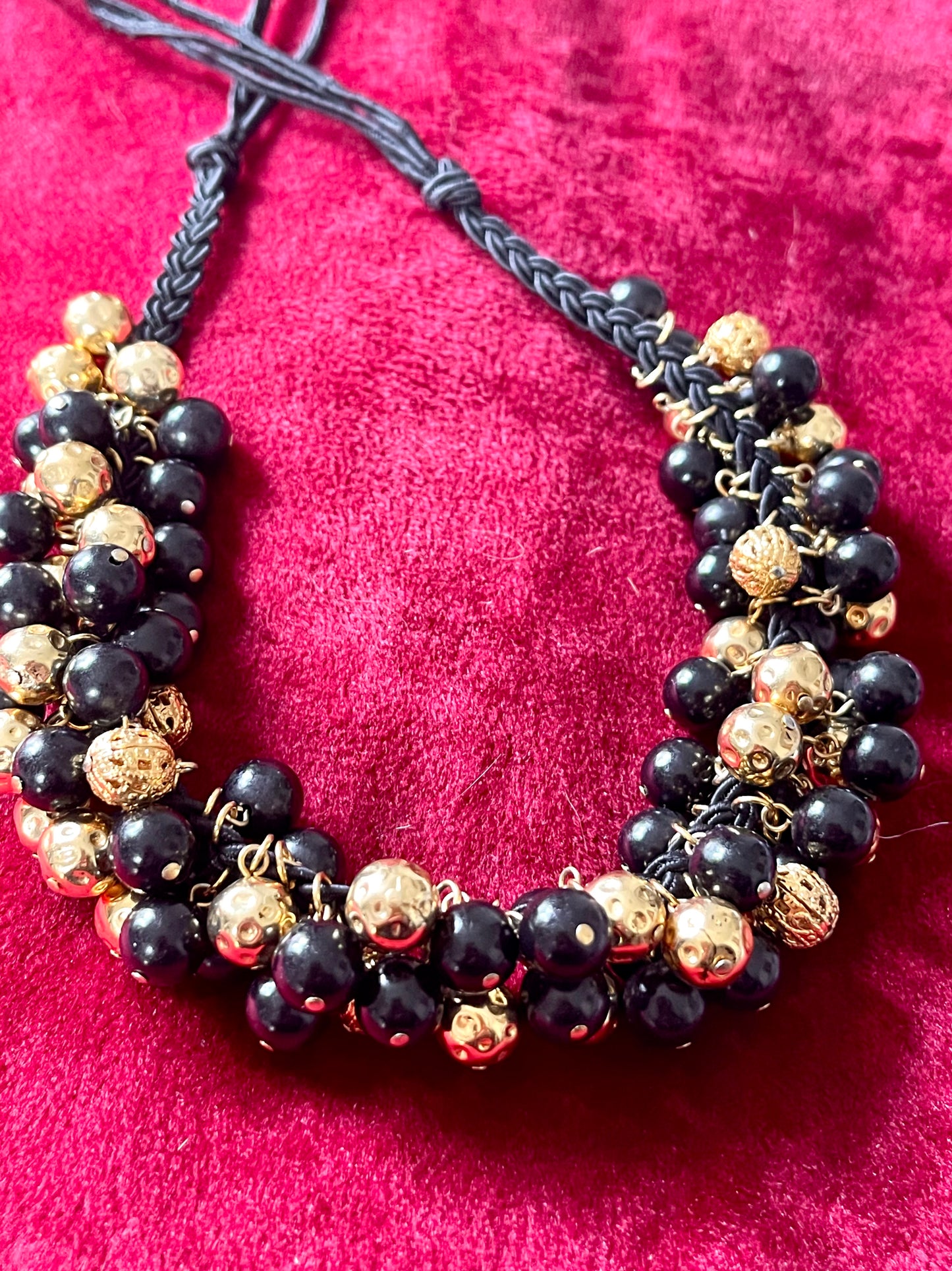Close up Vintage Yves Saint Laurent beaded necklace with black and gold beads, woven into braided black cotton cords, displayed on a red velvet background
