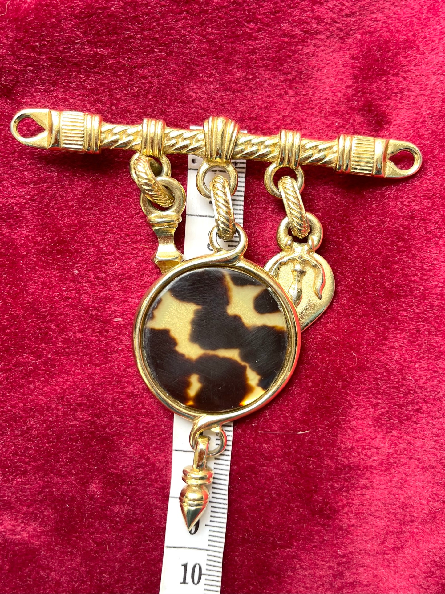 Using a measuring tape to show length of Luxury vintage brooch by Yves Saint Laurent displayed on red fabric surface, featuring signature animal print.