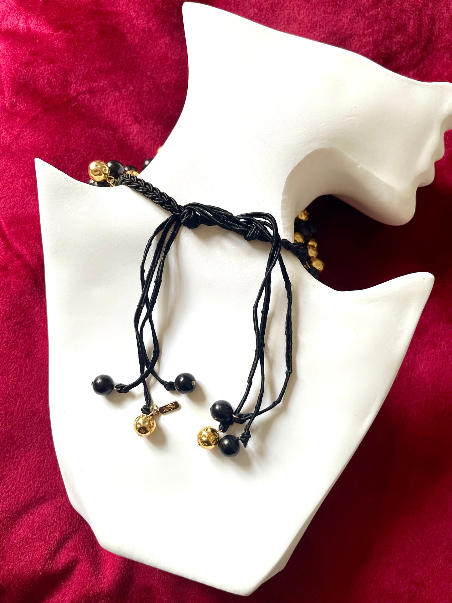 Back view with tag Vintage Yves Saint Laurent beaded necklace with black and gold beads, woven into braided black cotton cords, displayed on a red velvet background