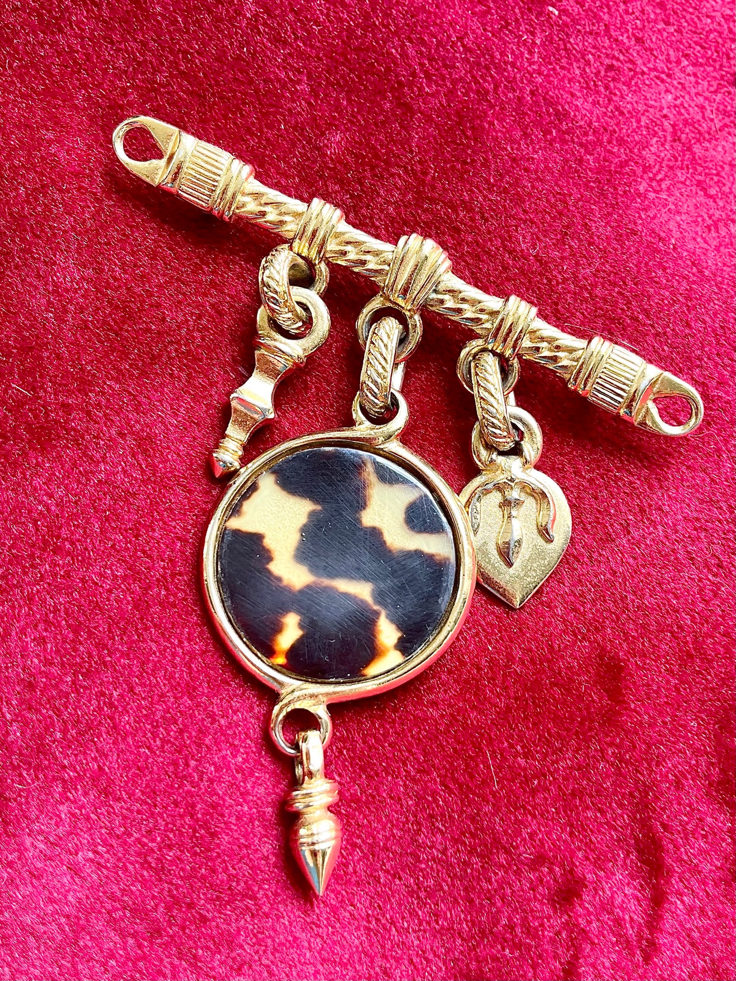 Yves Saint Laurent vintage brooch with gold detailing and leopard-print charm photographed on red velvet.