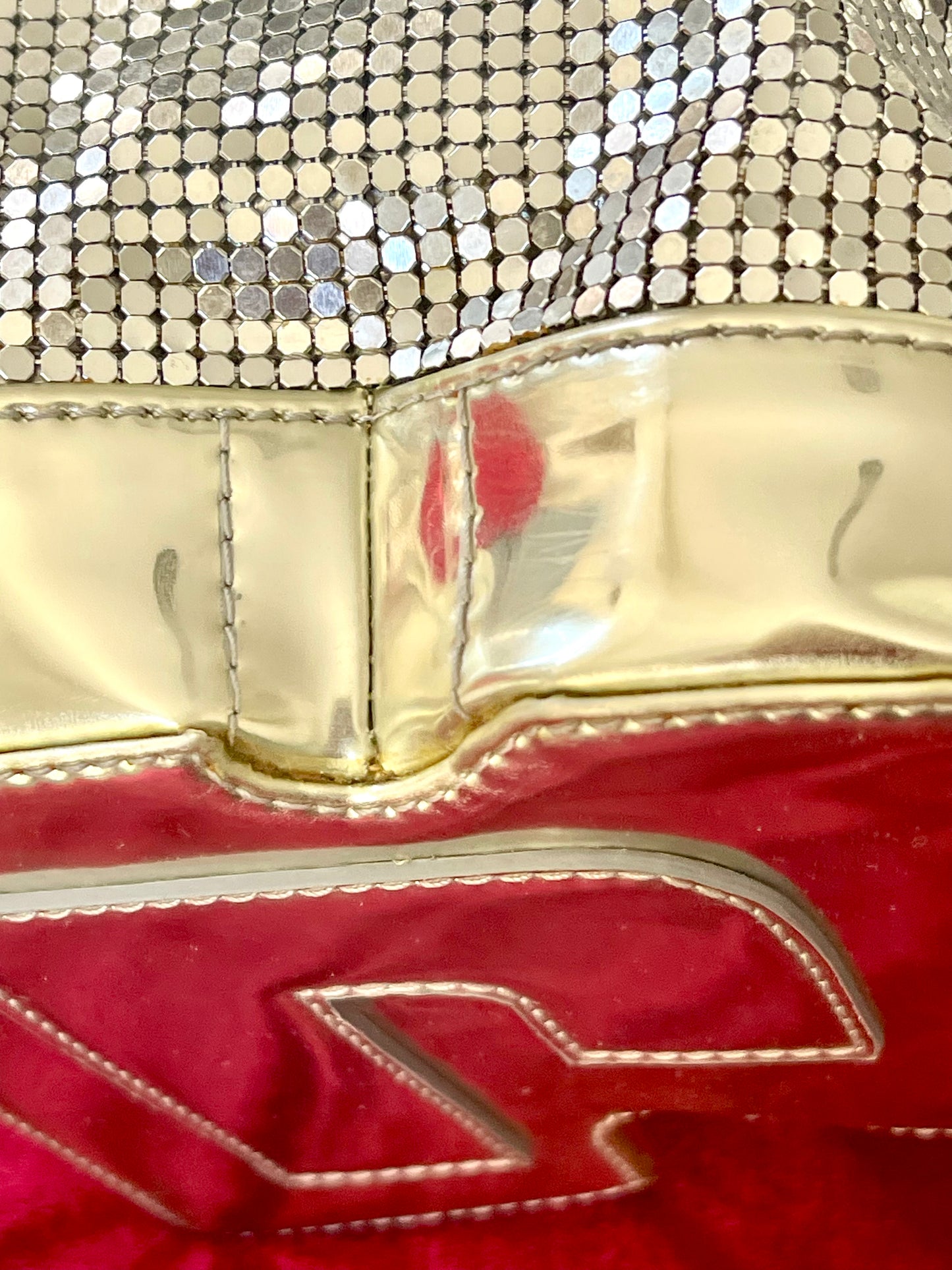Close up on signs of wear of Paco Rabanne silver shoulder/wrist bag with both straps shown, on red velvet fabric background.