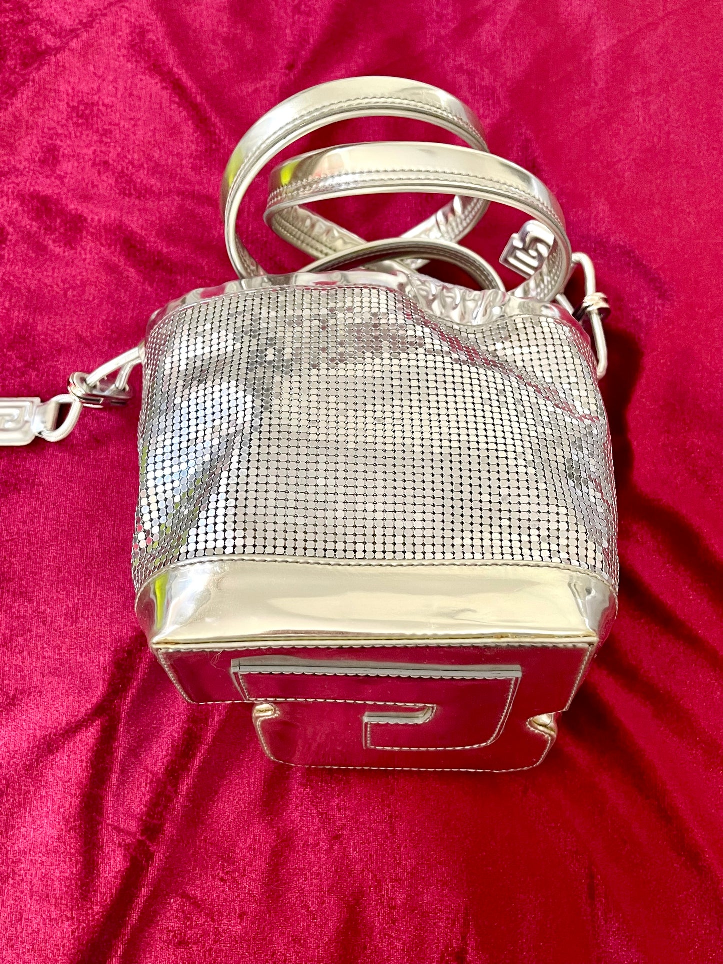Full view of Paco Rabanne silver shoulder/wrist bag with both straps shown, on red velvet fabric background.