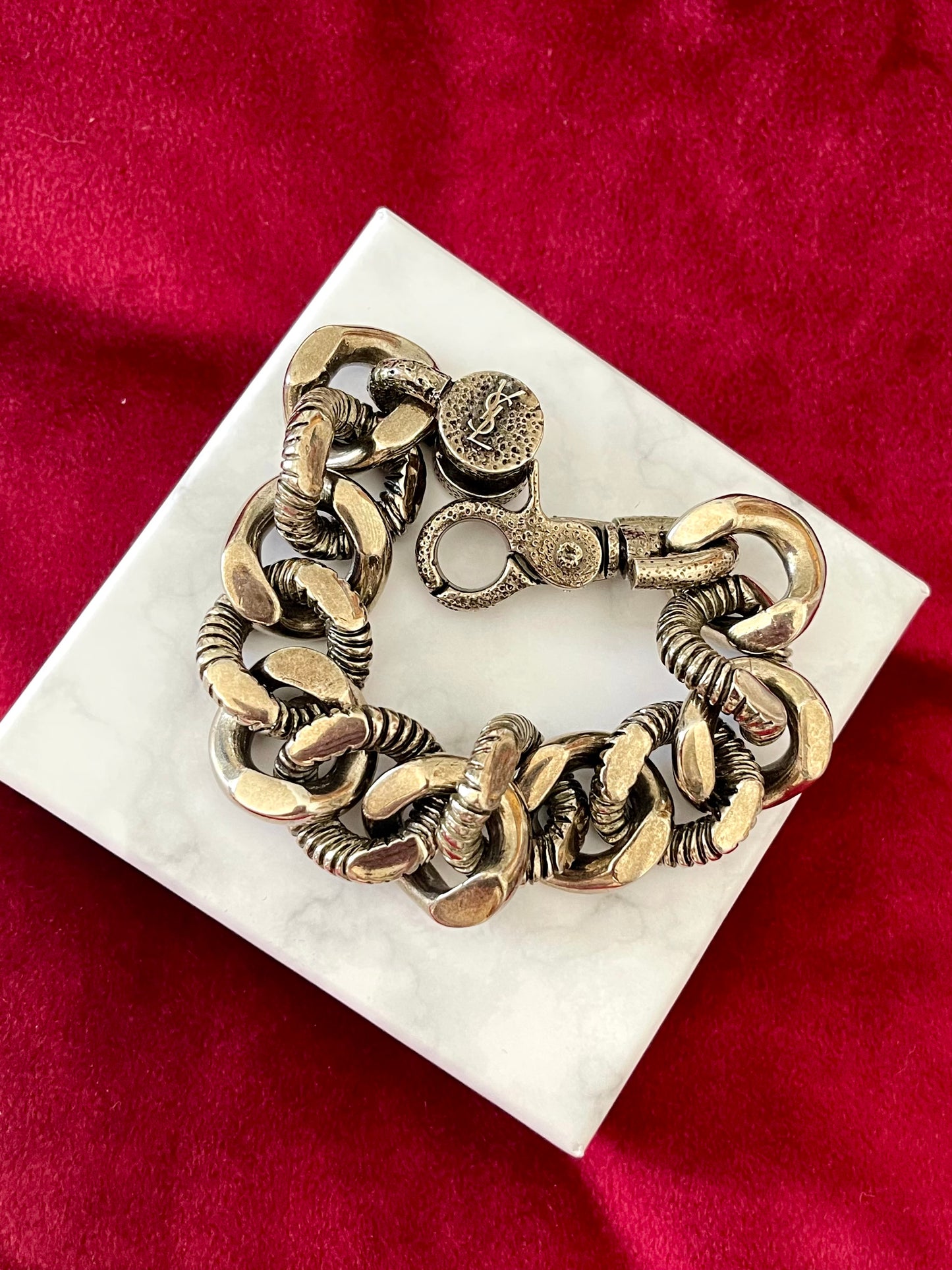 Top view Preloved YSL bronze and grey chain worn as a statement piece against white background with red velvet