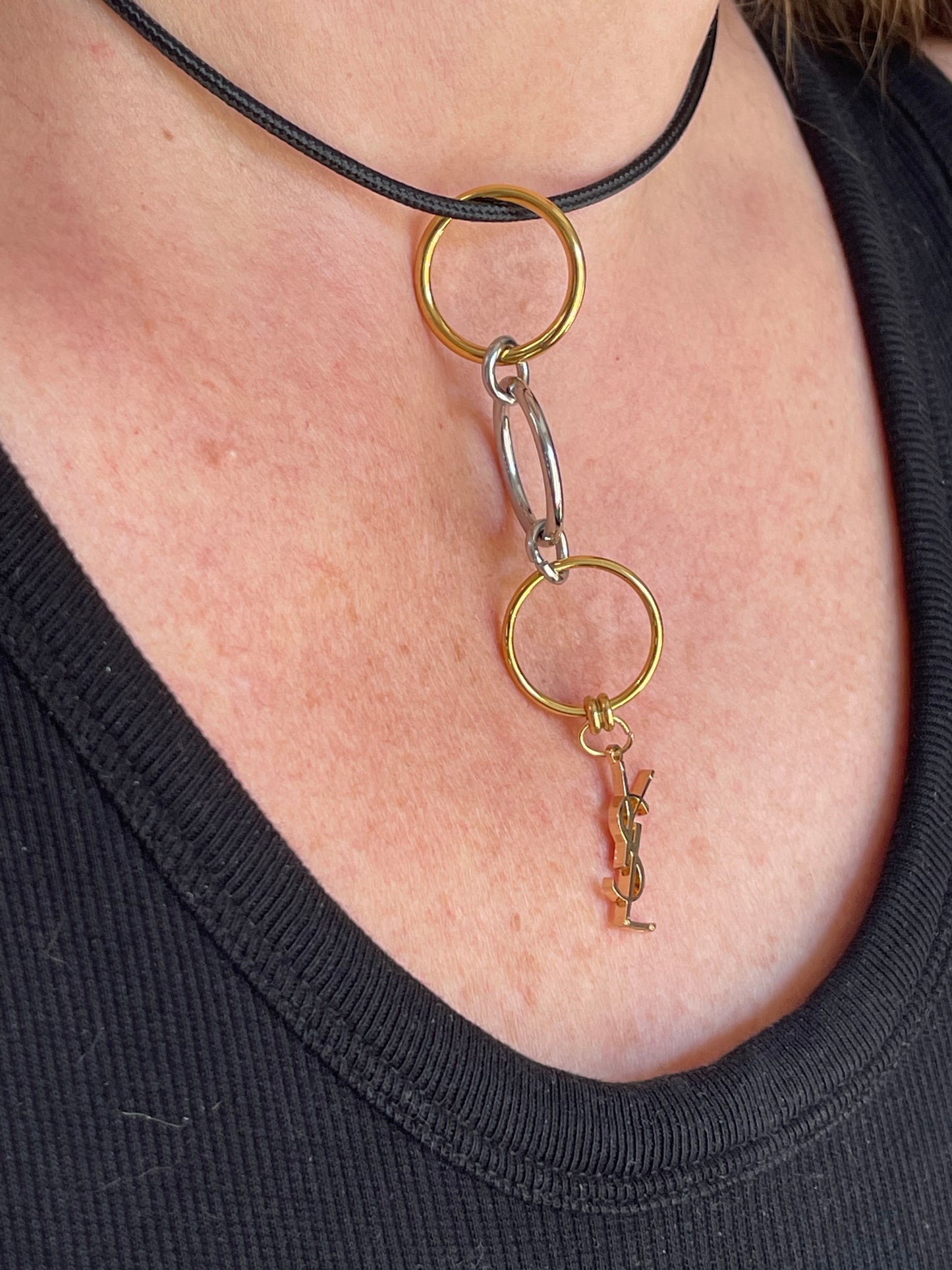 On hand close up view Yves Saint Laurent authentic charm as a ring pendant and bracelet with magnetic black cord stainless steel gold silver tone
