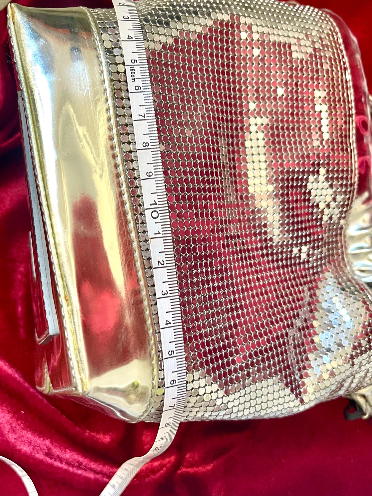 Showing width size view of Paco Rabanne silver shoulder/wrist bag with both straps shown, on red velvet fabric background using a measuring tape