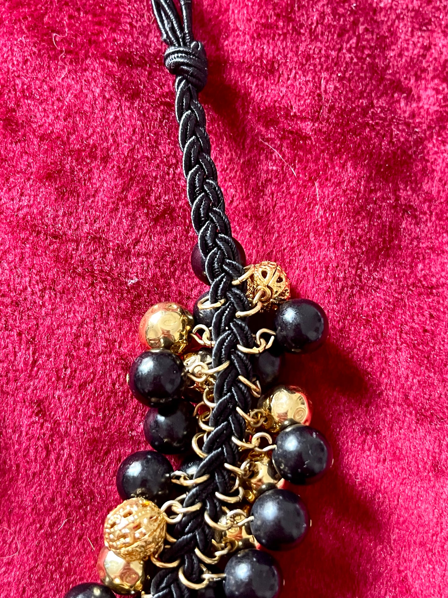 Close up Vintage Yves Saint Laurent beaded necklace with black and gold beads, woven into braided black cotton cords, displayed on a red velvet background