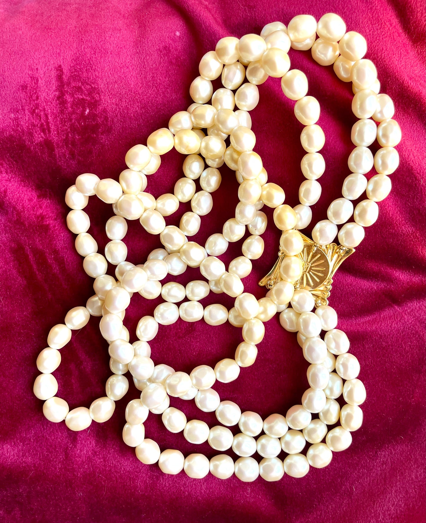 Close-up of gold-tone sculptural clasp with domed faux pearl on a vintage YSL pearl necklace, held in hand to show detail and hallmark