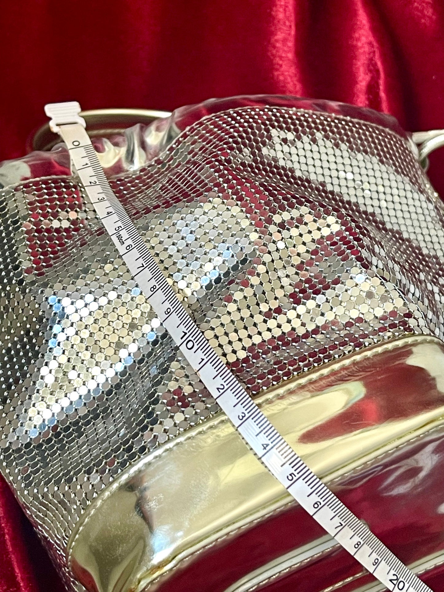 Length view of Paco Rabanne silver shoulder/wrist bag with both straps shown, on red velvet fabric background with measuring tape