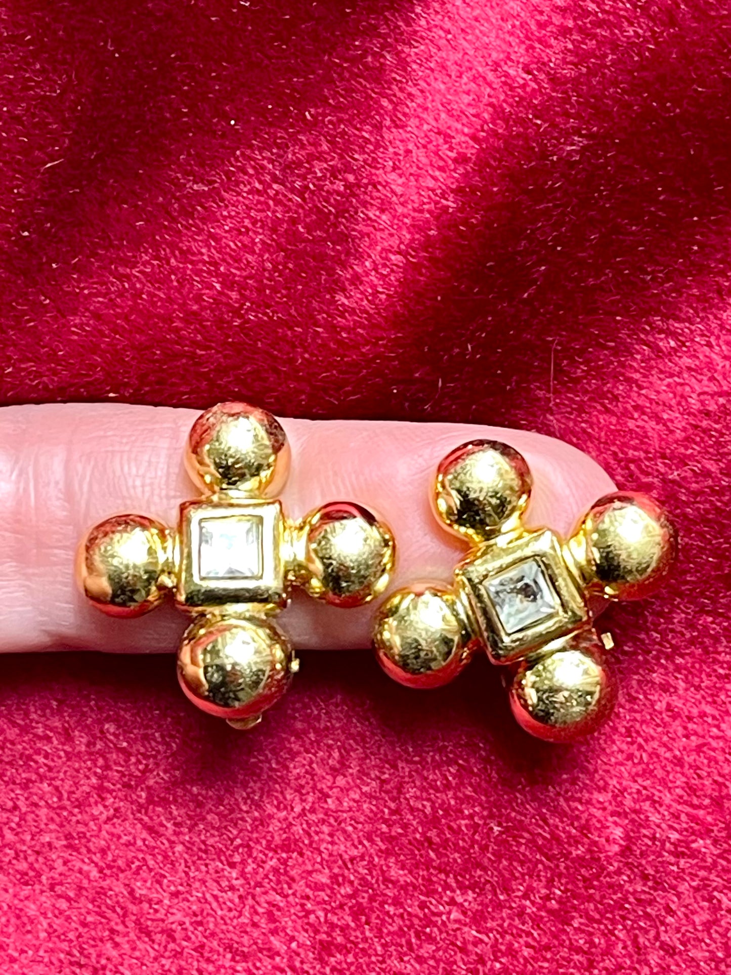 Yves Saint Laurent vintage gold tone cross clip-on earrings from the 1980s held in hand, showing rounded gold domes and square-cut center stones