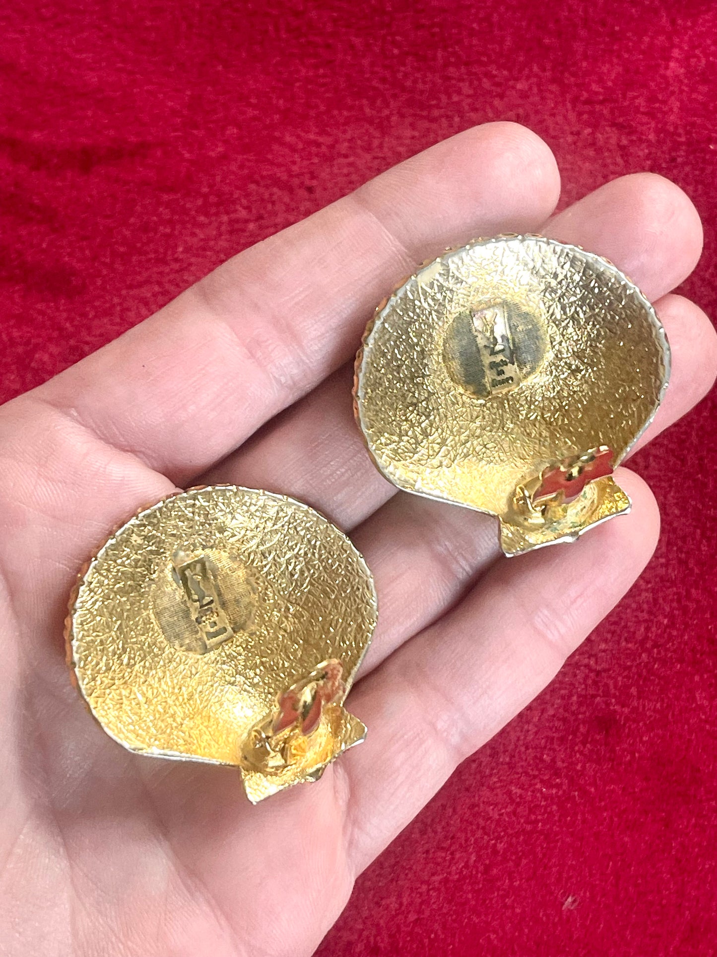 Back side view Gold-tone 80s vintage Yves Saint Laurent shell-shaped earrings displayed on hand and a red fabric showing detailed signature and hallmark