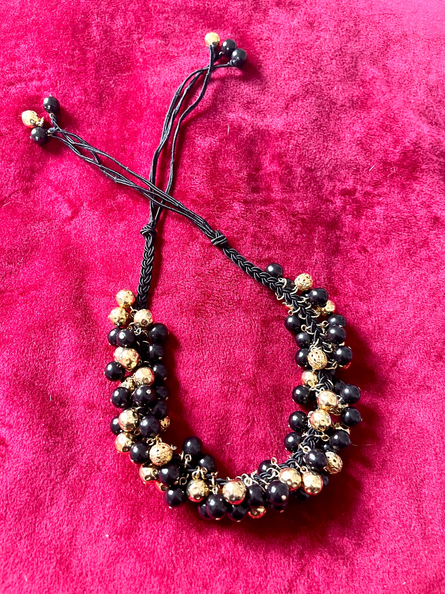 Vintage Yves Saint Laurent beaded necklace with black and gold beads, woven into braided black cotton cords, displayed on a red velvet background