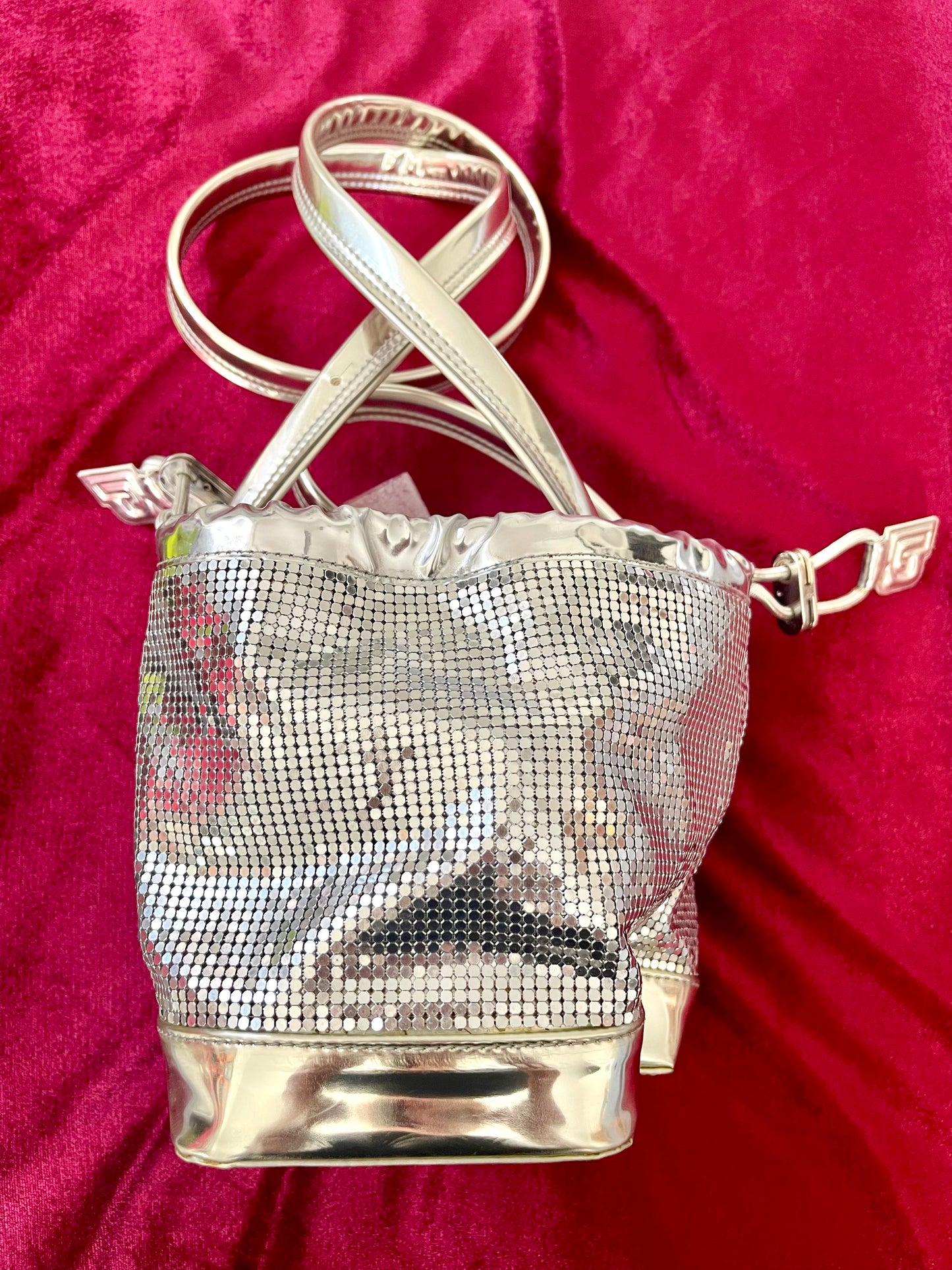 Full view of Paco Rabanne silver shoulder/wrist bag with both straps shown, on red velvet fabric background.