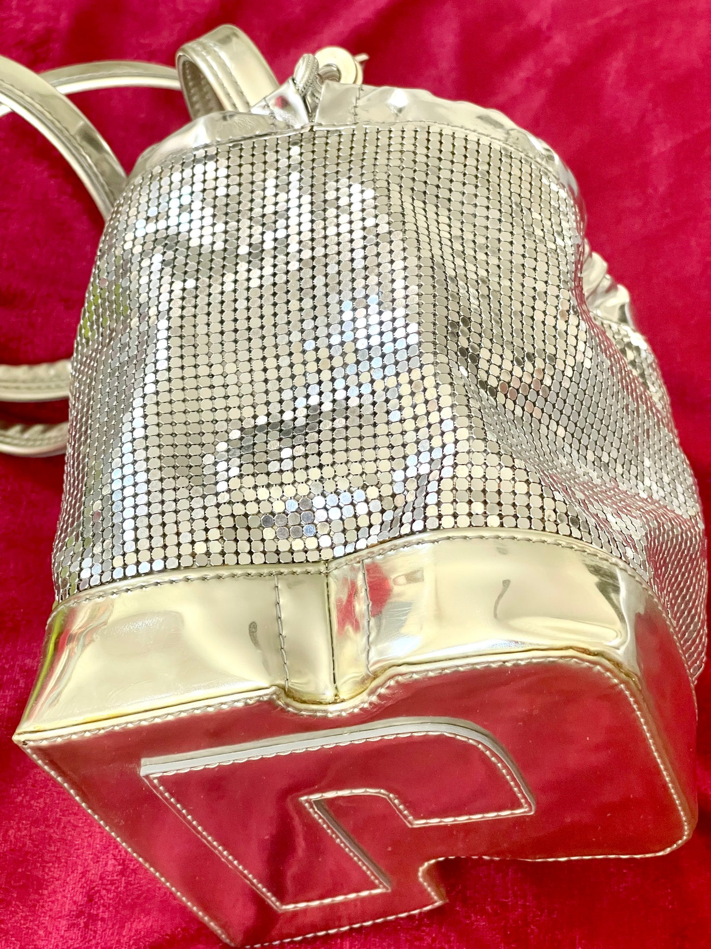 Side view of Paco Rabanne silver shoulder/wrist bag with both straps shown, on red velvet fabric background.