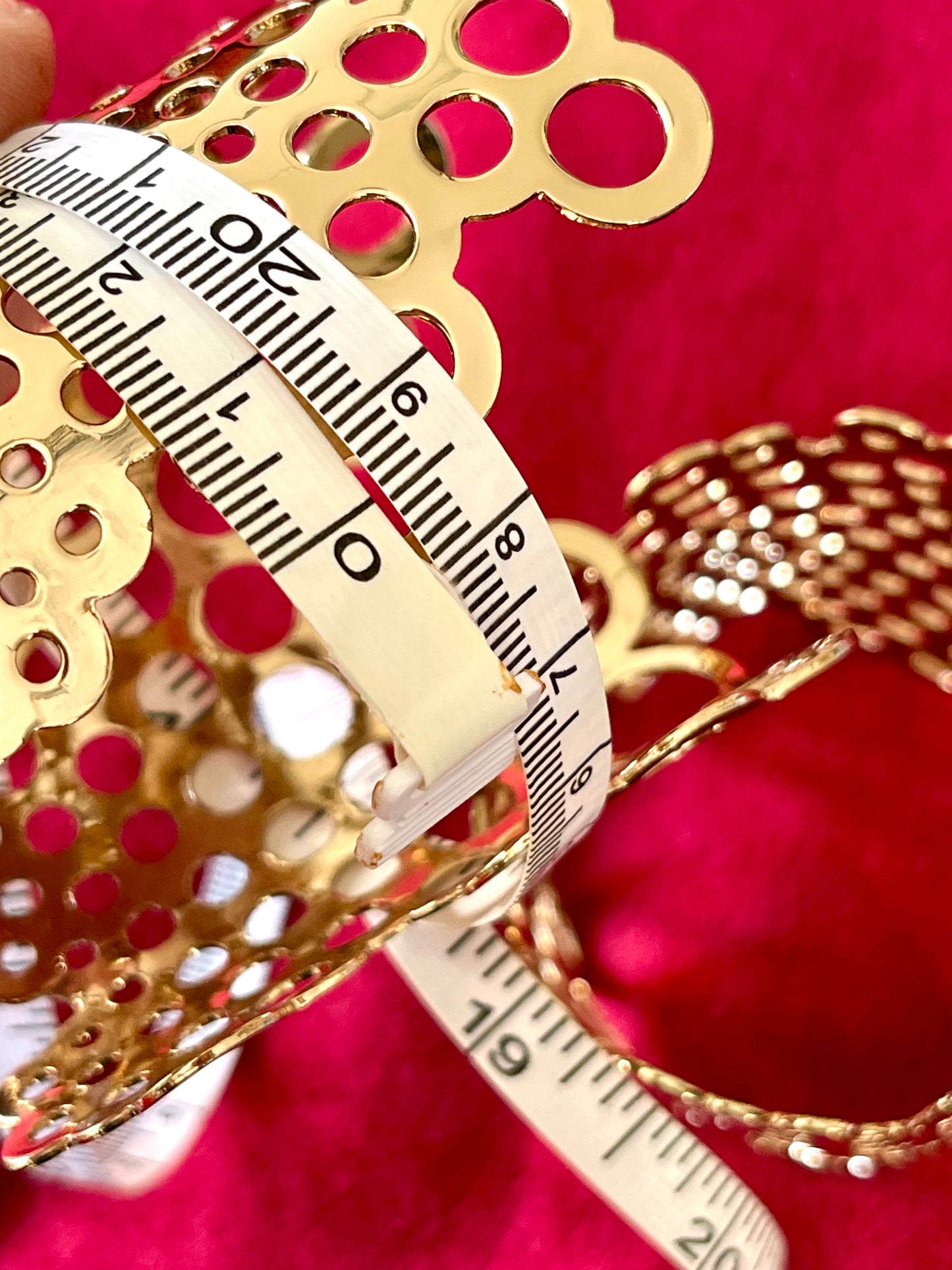 18 cm Paco Rabanne gold-tone vintage cuff bracelets displayed on rich red velvet fabric, highlighting their texture and sculptural form using a measuring tape