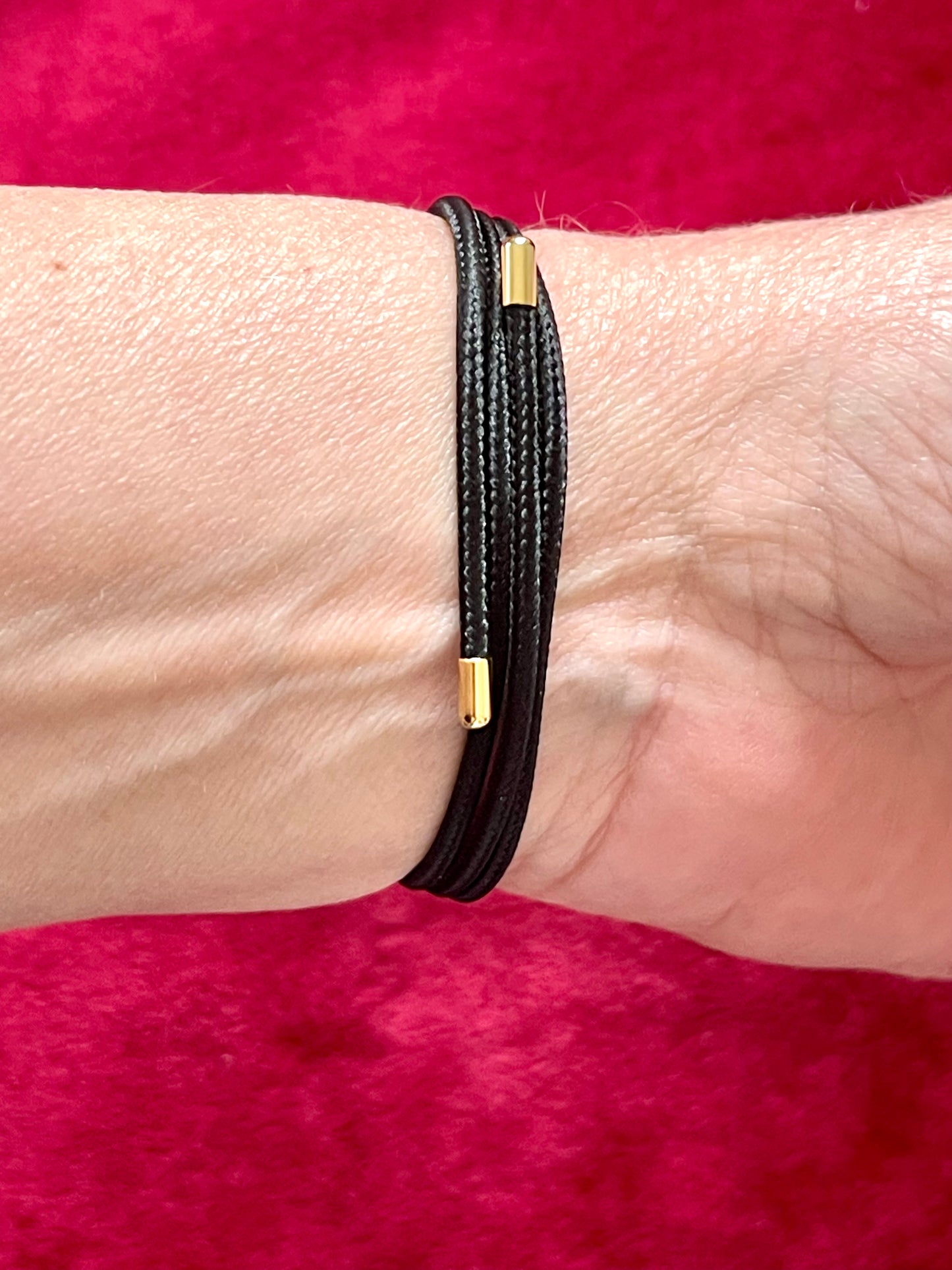 Back view of magnetic cord showcasing the adjustable size On hand close up view Yves Saint Laurent authentic charm as a ring pendant and bracelet with magnetic black cord stainless steel gold silver tone