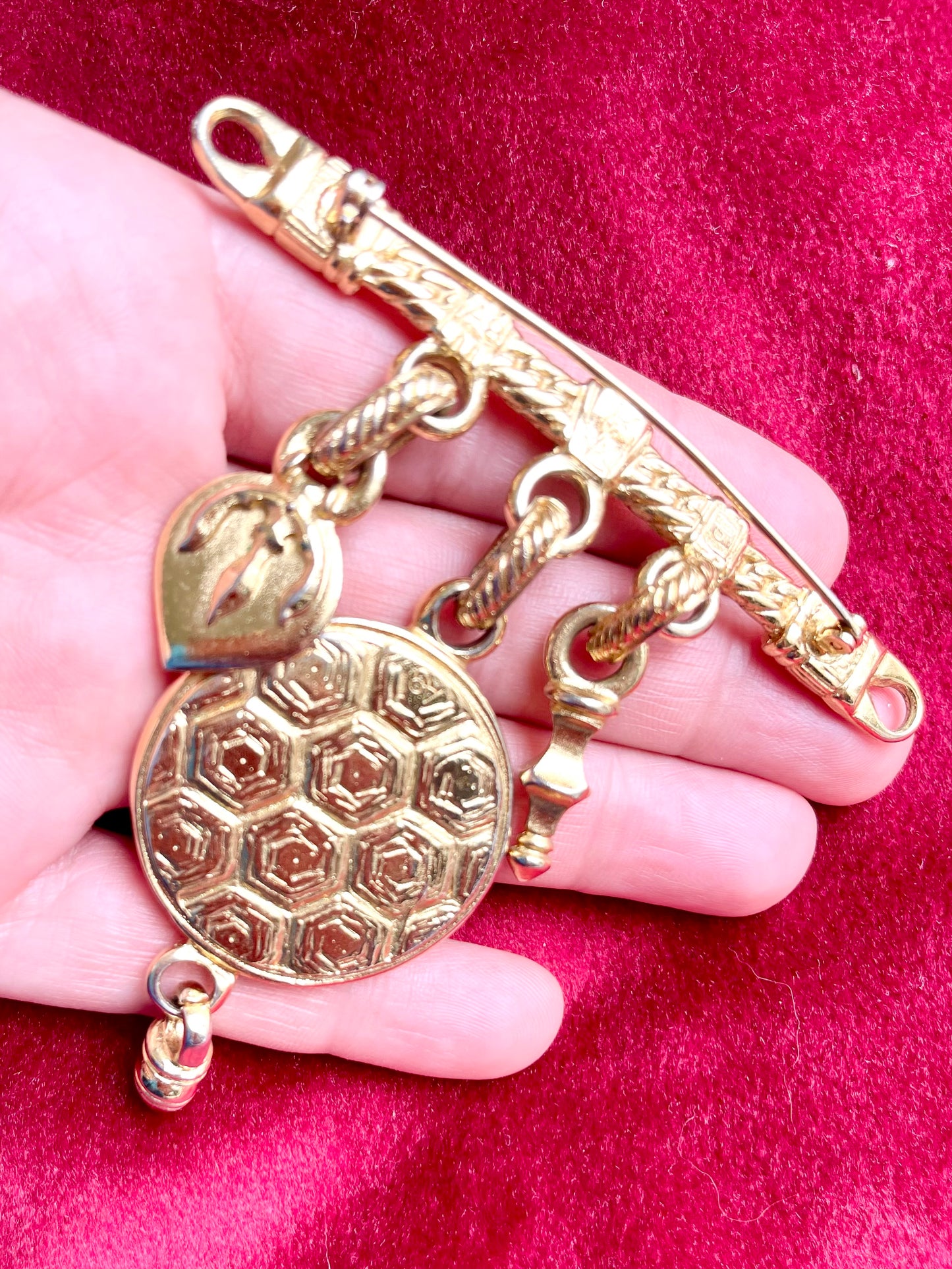 Hand holding a YSL gold-tone brooch featuring leopard cabochon and hanging charms, back view