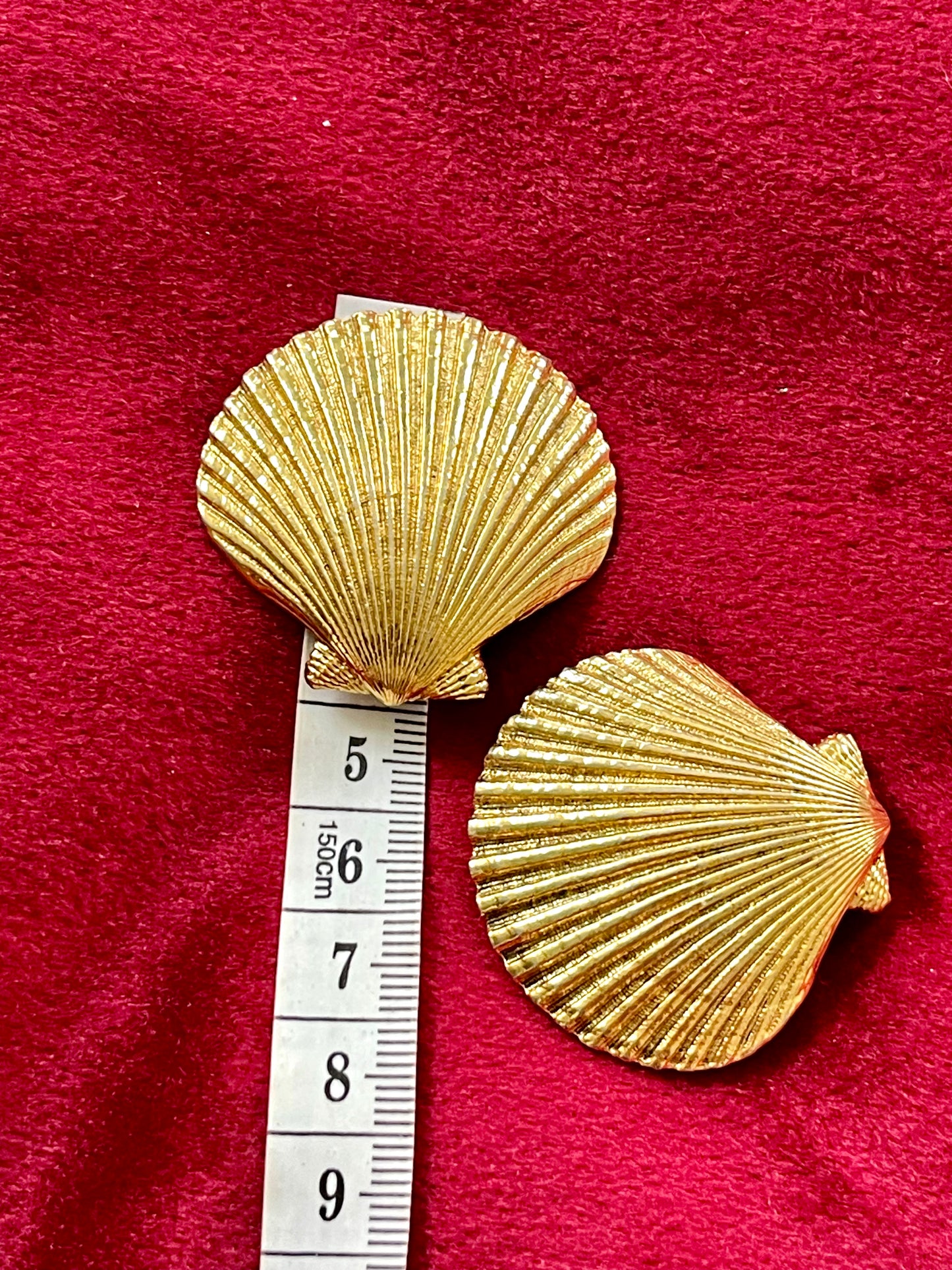 Vintage YSL gold-tone shell-shaped earrings displayed on red fabric with measuring tape, textured surface in excellent condition.