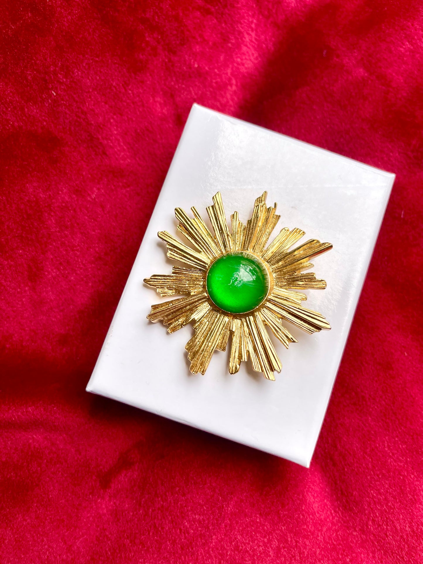 Vintage Yves Saint Laurent 1980s gold-tone sunburst brooch with green cabochon center on white display