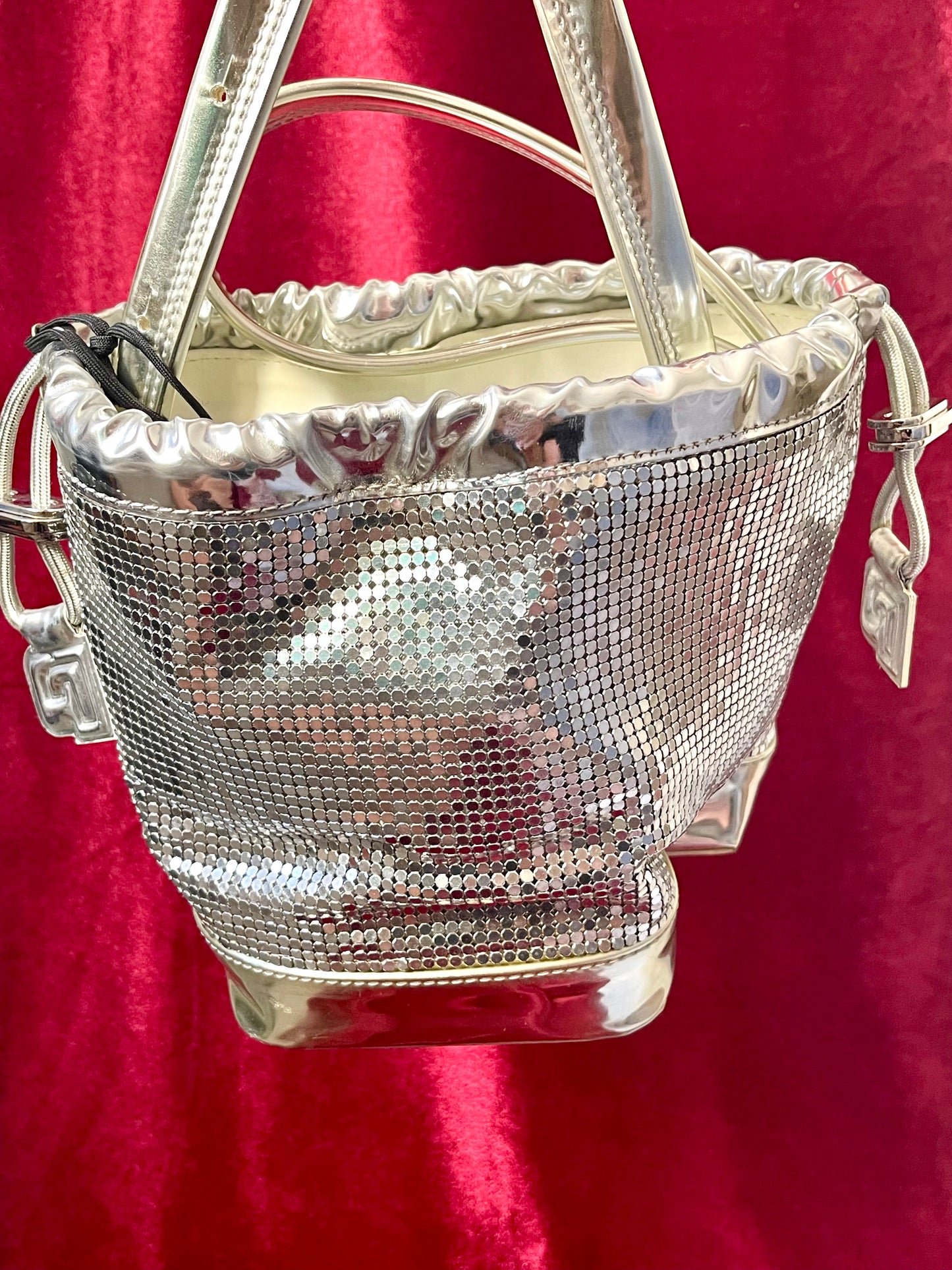 Close up Full view of Paco Rabanne silver shoulder/wrist bag with both straps shown, on red velvet fabric background.