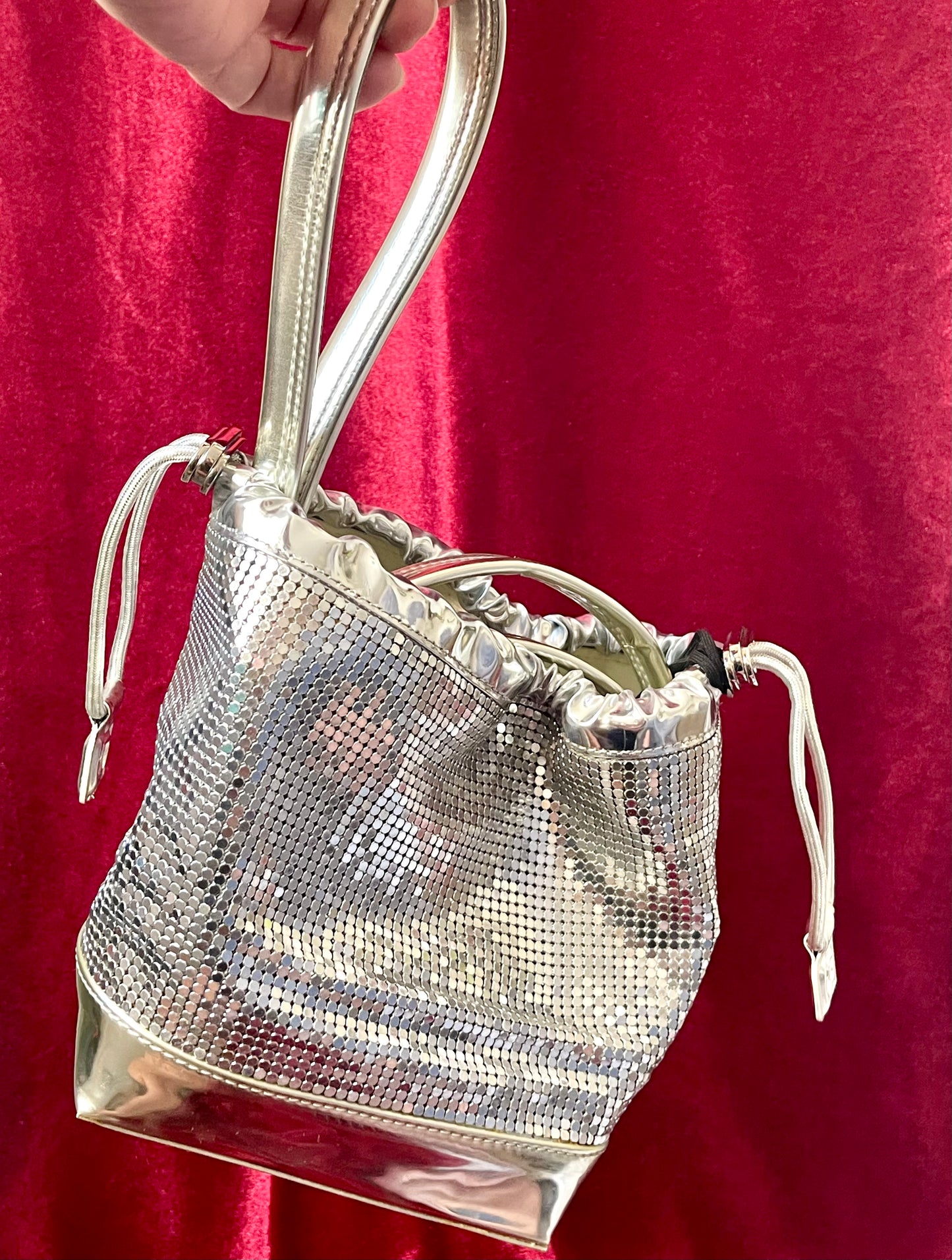 Using the top handle strap close up view of Paco Rabanne silver shoulder/wrist bag with both straps shown, on red velvet fabric background.