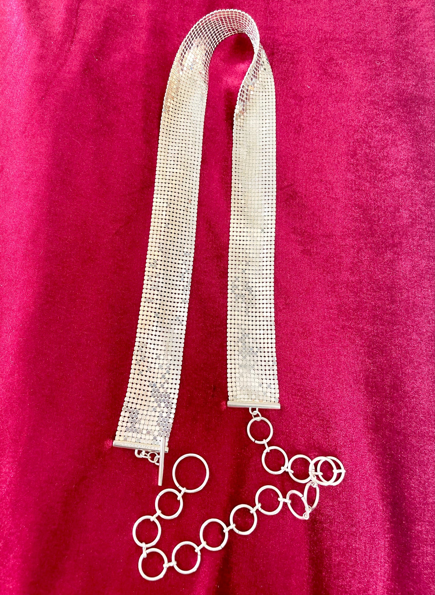 Flat lay vintage silver Paco Rabanne mesh belt on red velvet background.
