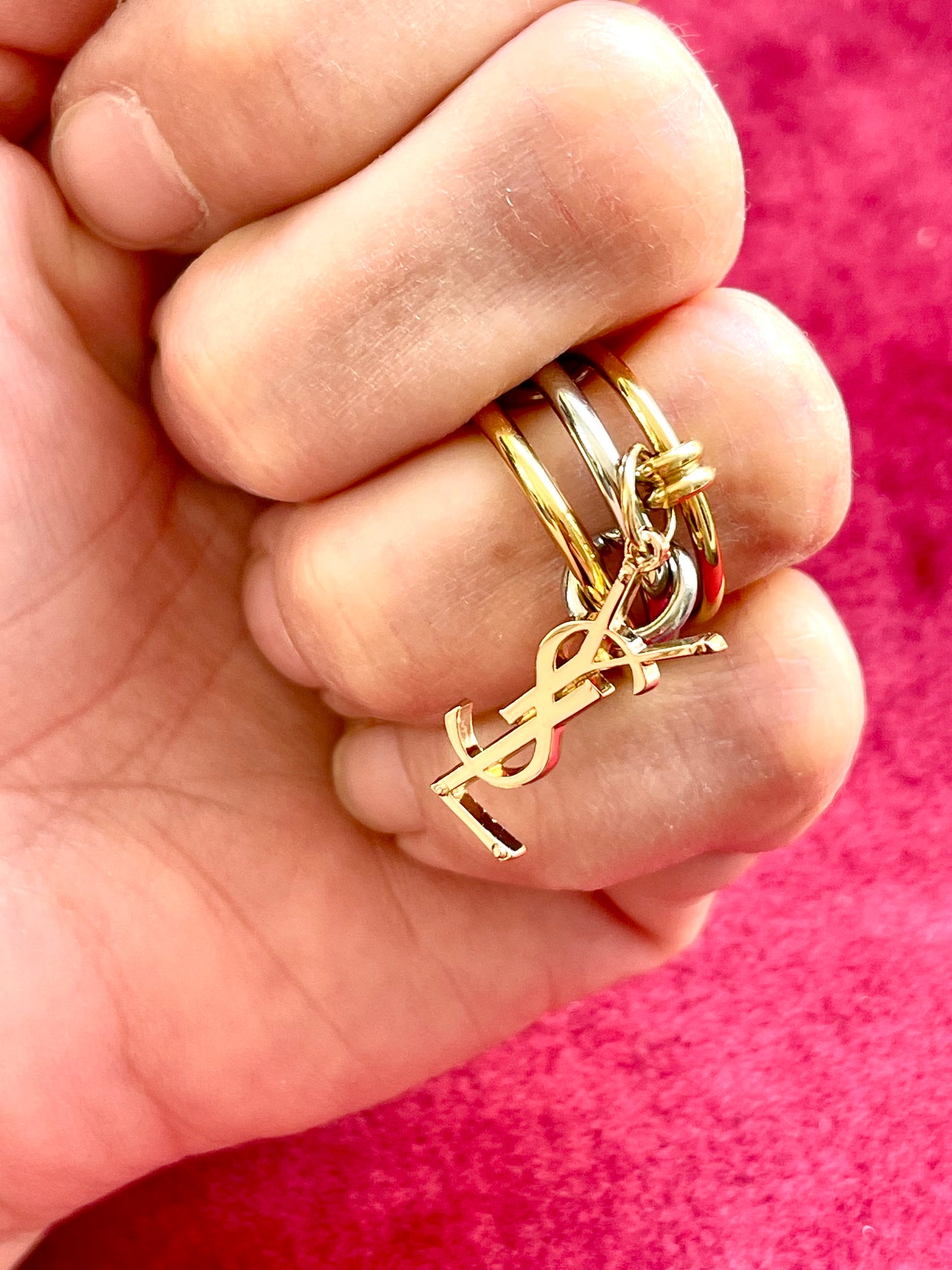 On hand close up view Yves Saint Laurent authentic charm as a ring pendant and bracelet with magnetic black cord stainless steel gold silver tone