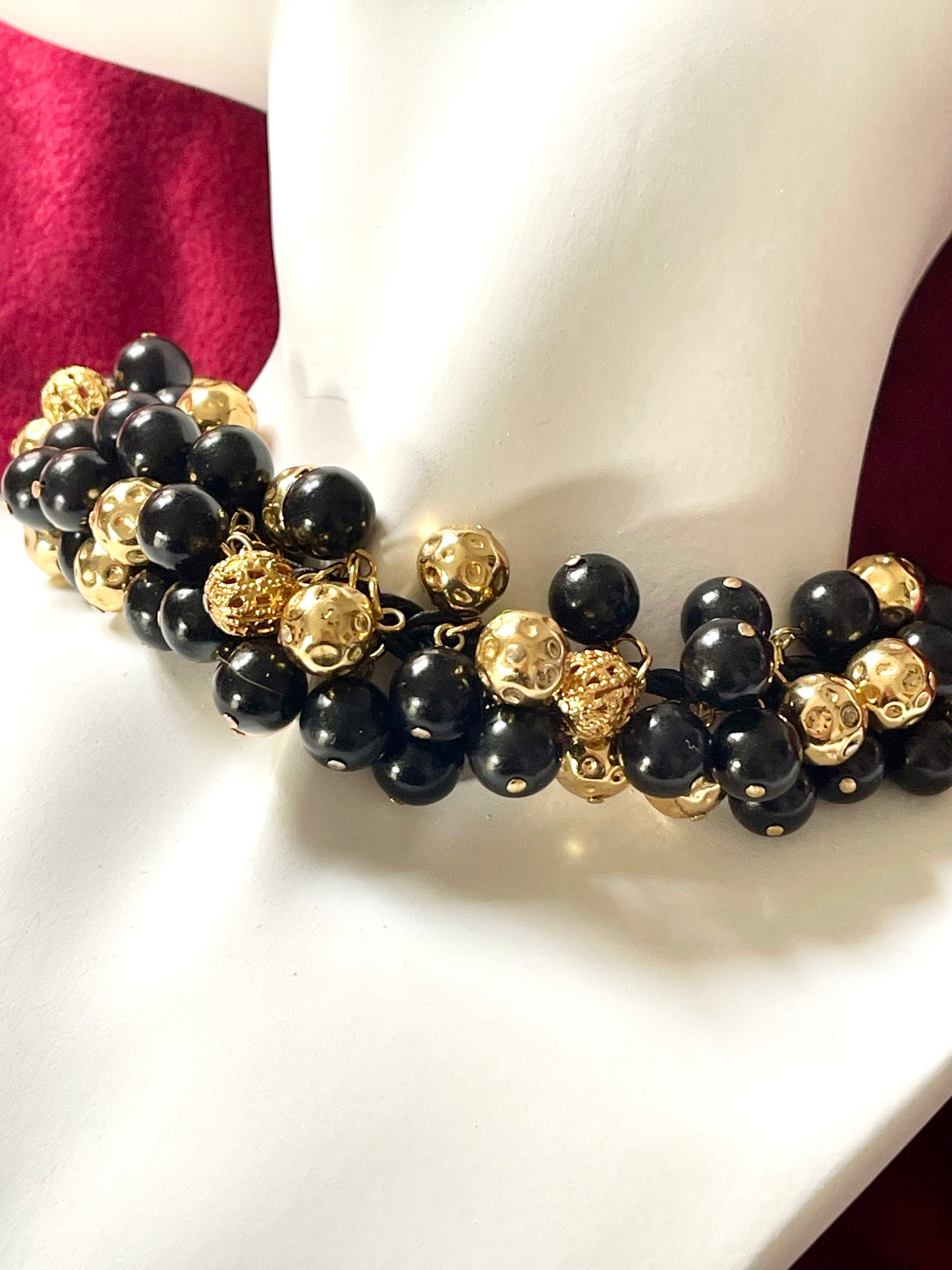 Close up on Vintage Yves Saint Laurent beaded necklace with black and gold beads, woven into braided black cotton cords, displayed on a red velvet background