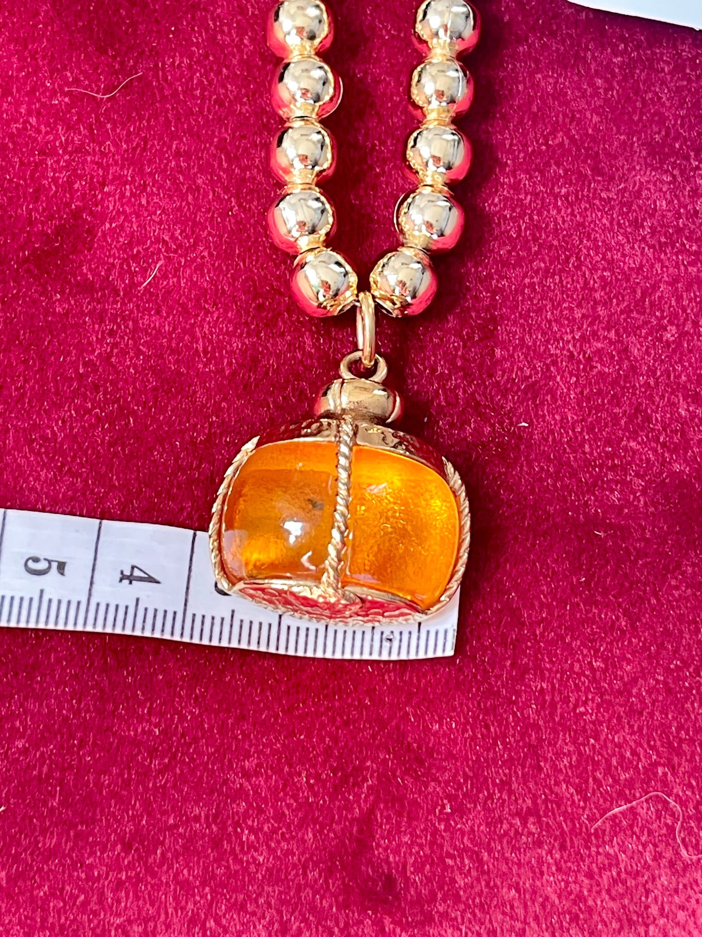 Front view of YSL vintage Champagne pendant with gold-plated finish, color-shifting in natural light showing size 3cm using a measuring tape