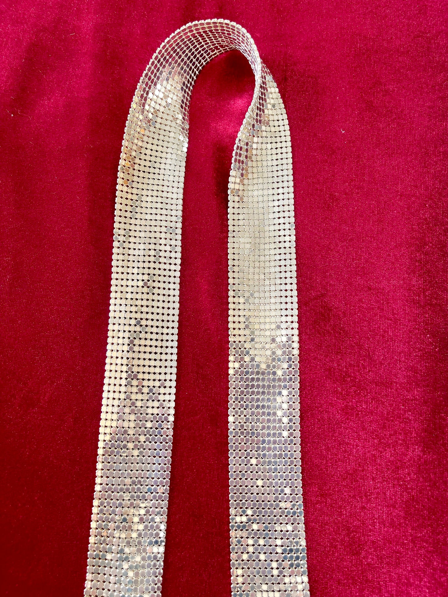 Flat lay of vintage silver Paco Rabanne mesh belt on red velvet background.